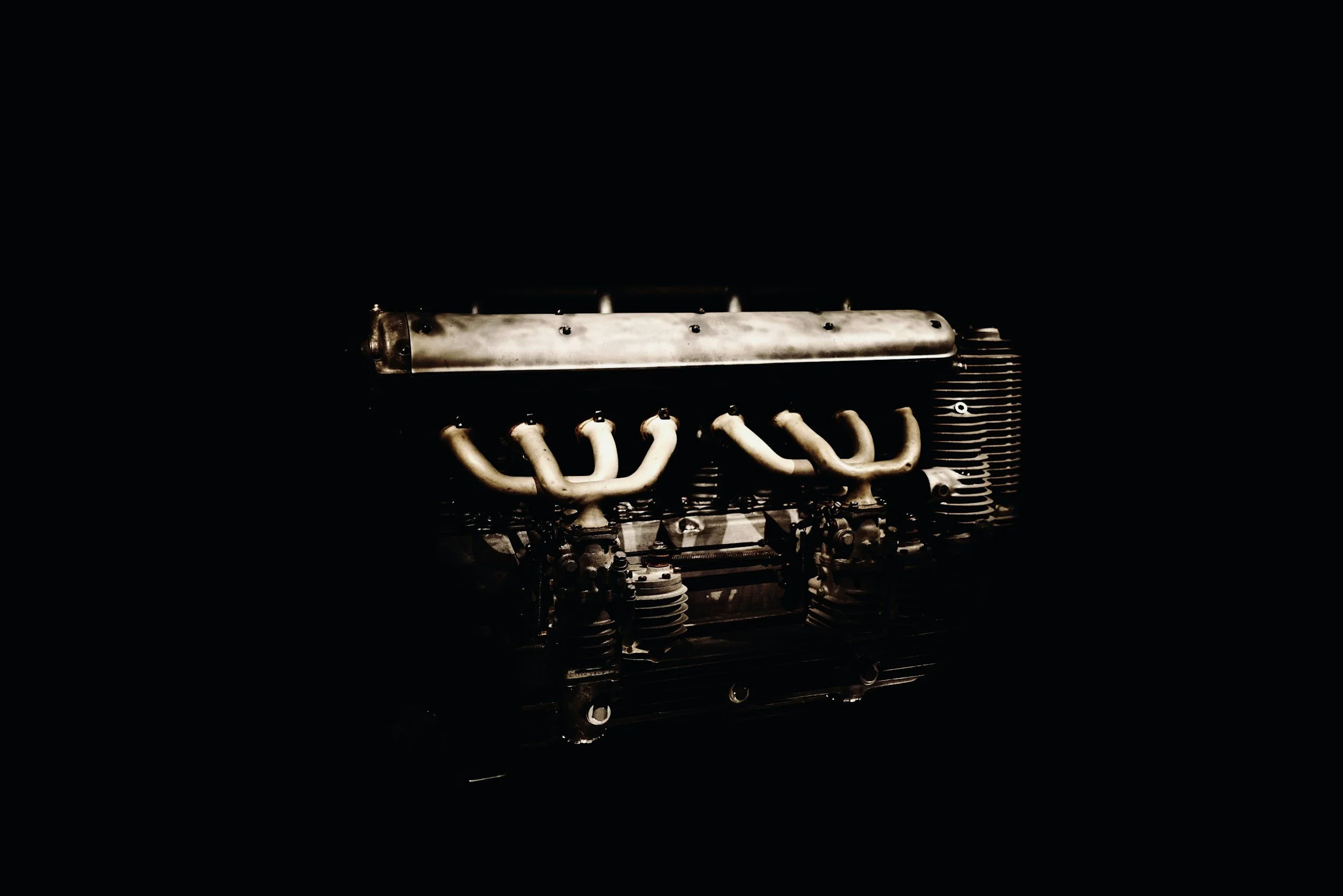 An old, vintage engine part with metal pipes and fins on a dark background.