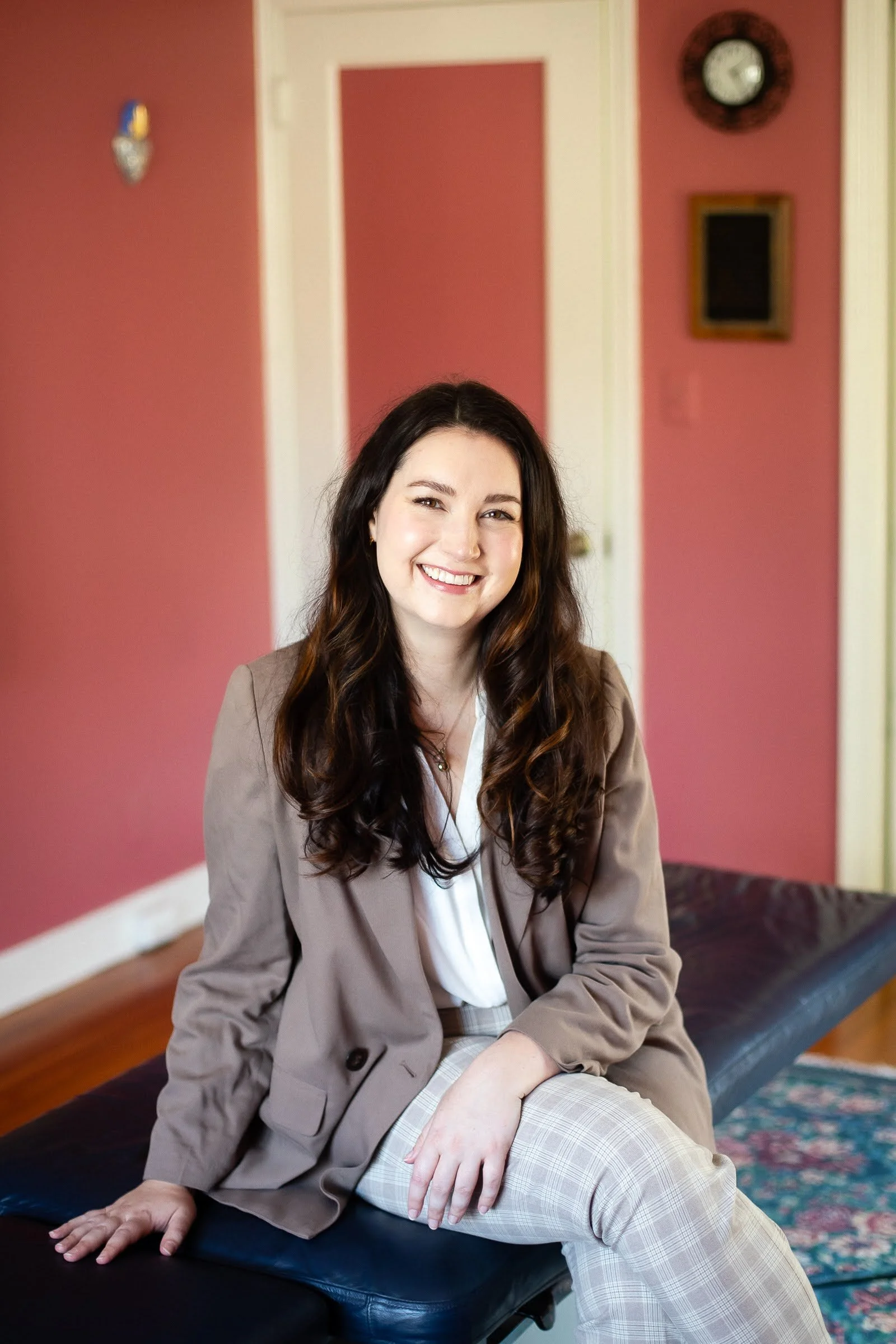 Dr. Kate Palmer sitting on a black examination table in a room with pink walls and a colorful rug