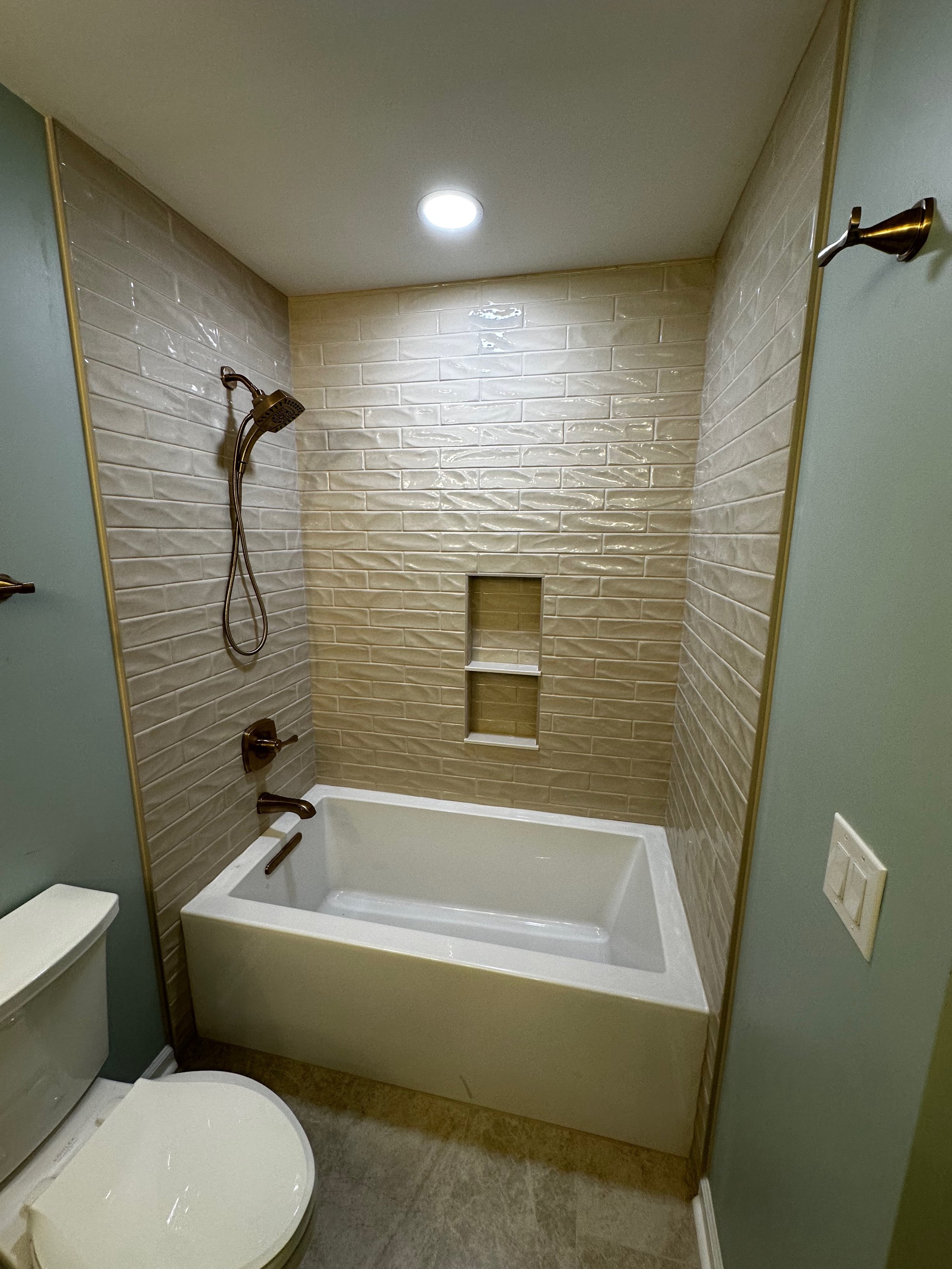 Bathroom with a bathtub, beige tiled wall, showerhead, and a toilet in the foreground.