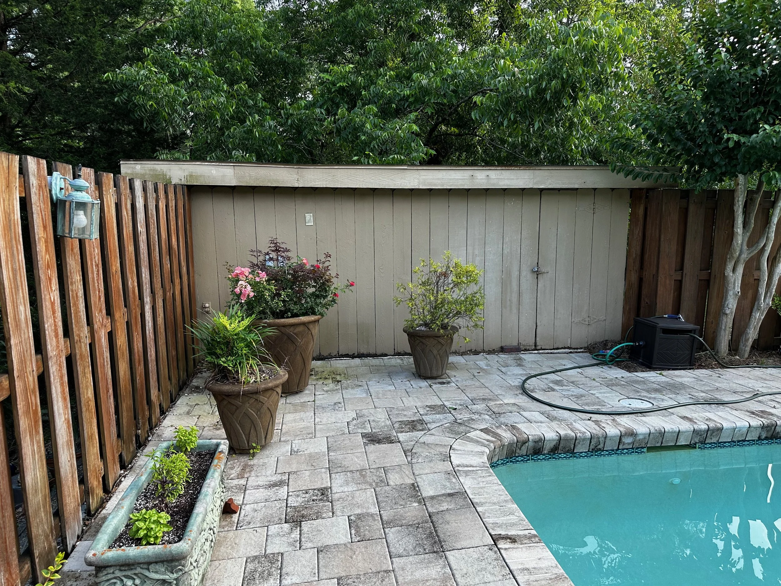 Backyard patio with a swimming pool, potted plants, and a wooden fence