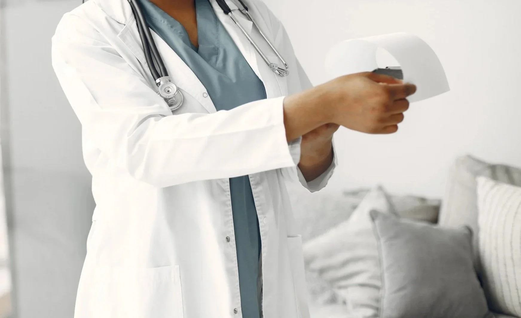 A healthcare professional in a white coat and stethoscope holding an X-ray of a chest.