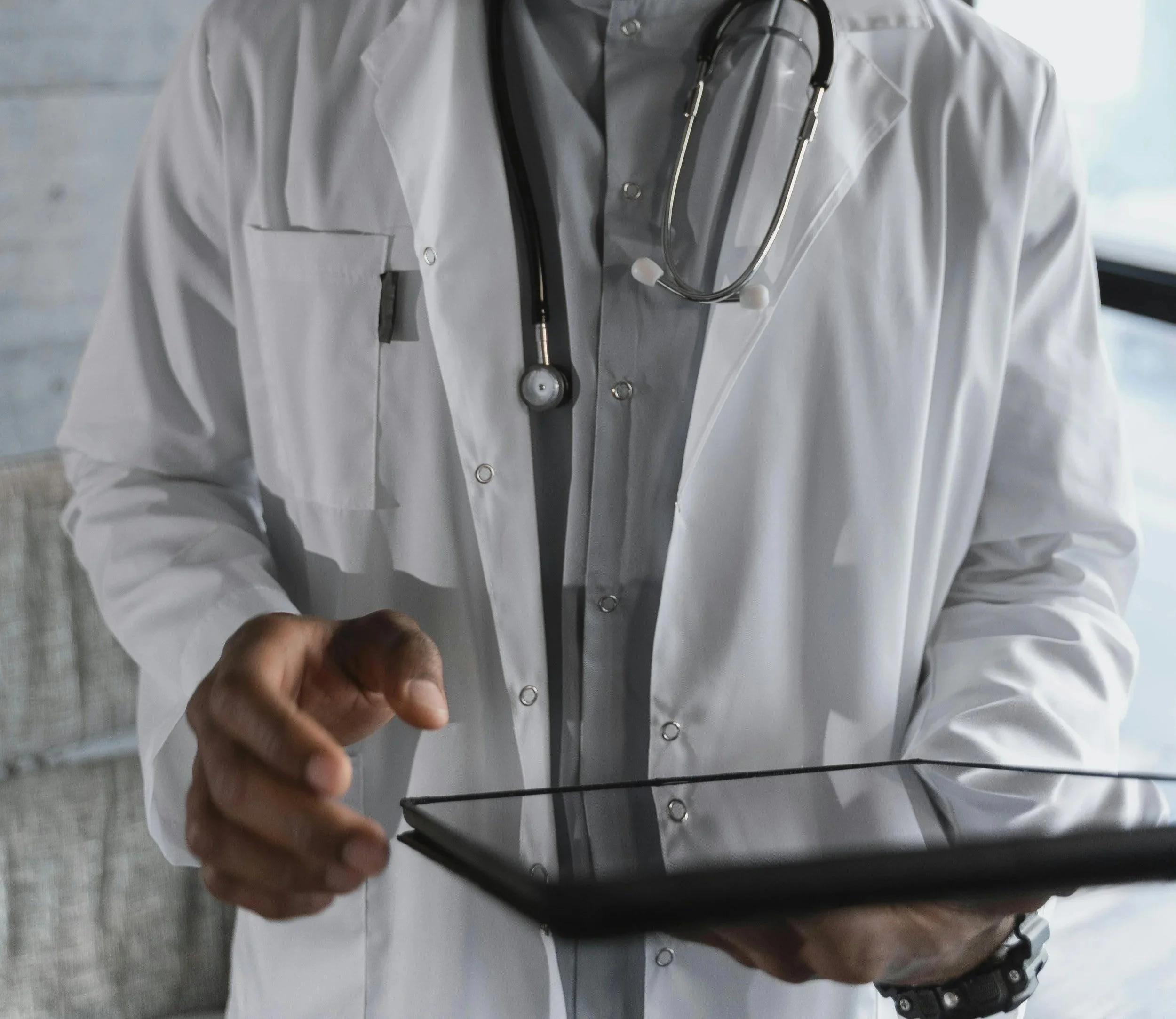 Person wearing a white lab coat with a stethoscope around their neck, holding a smartphone, taking a selfie through a mirror.