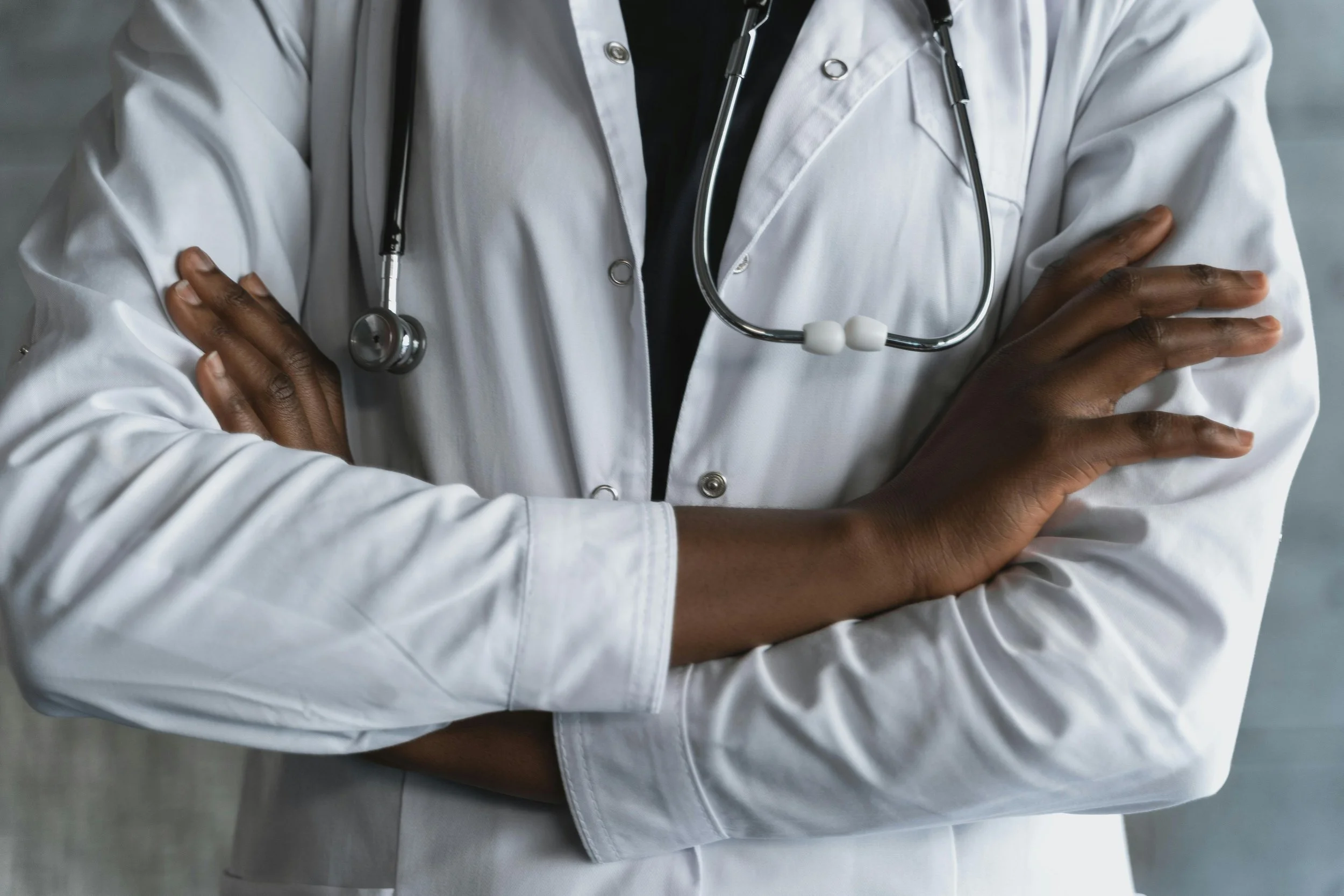 Close-up of a healthcare professional wearing a white lab coat and stethoscope with arms crossed.