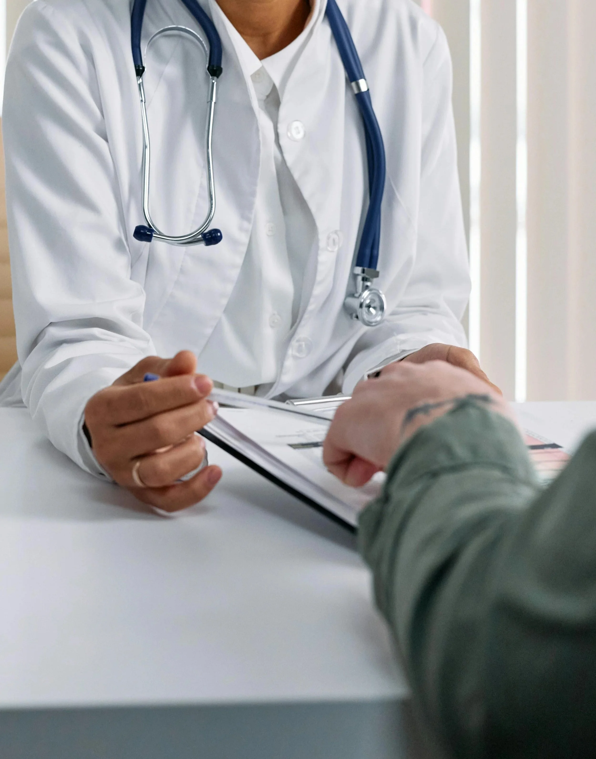 Doctor in white coat with stethoscope talking to a patient and taking notes.