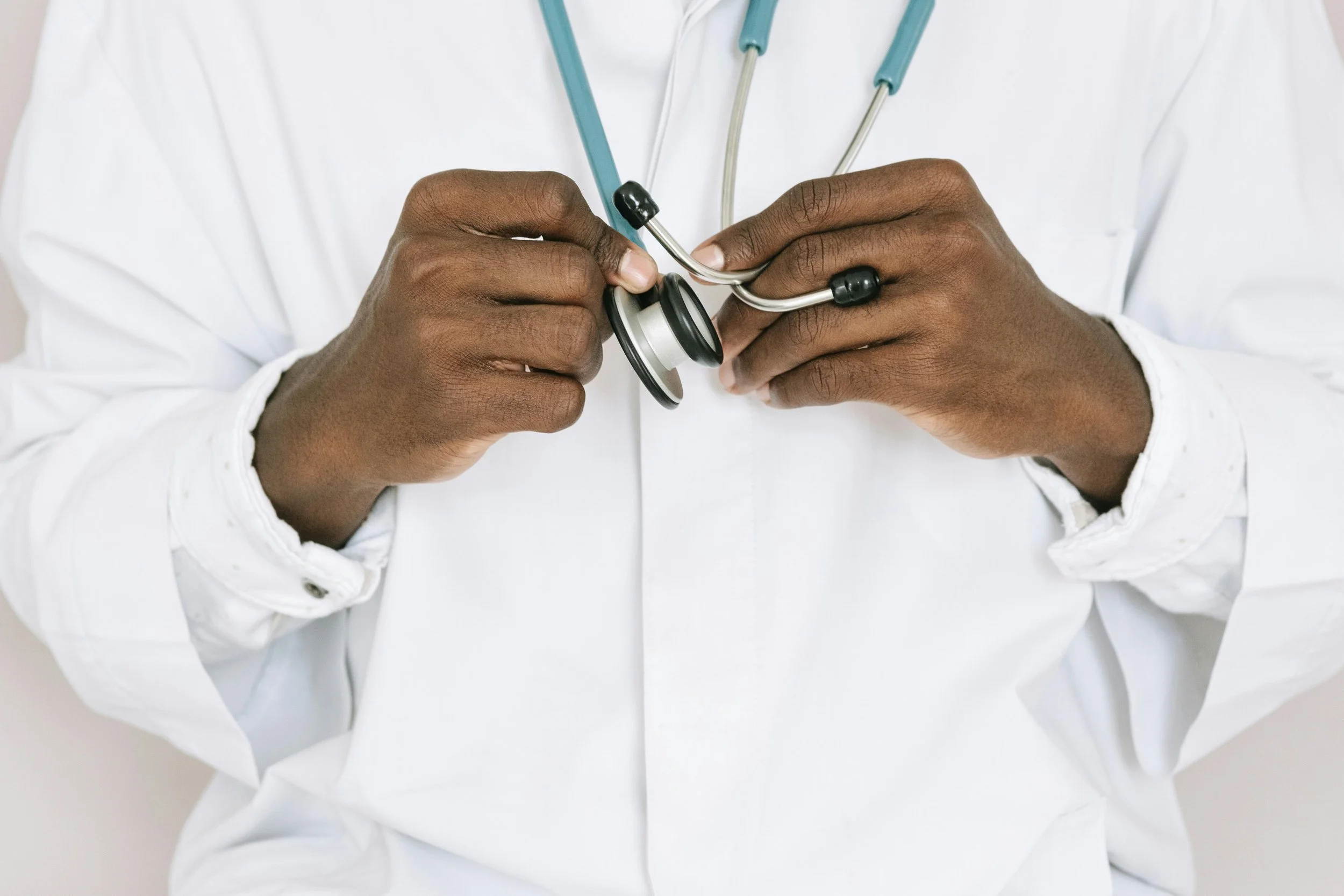 Close-up of a healthcare professional's hands adjusting a stethoscope, wearing a white medical coat.