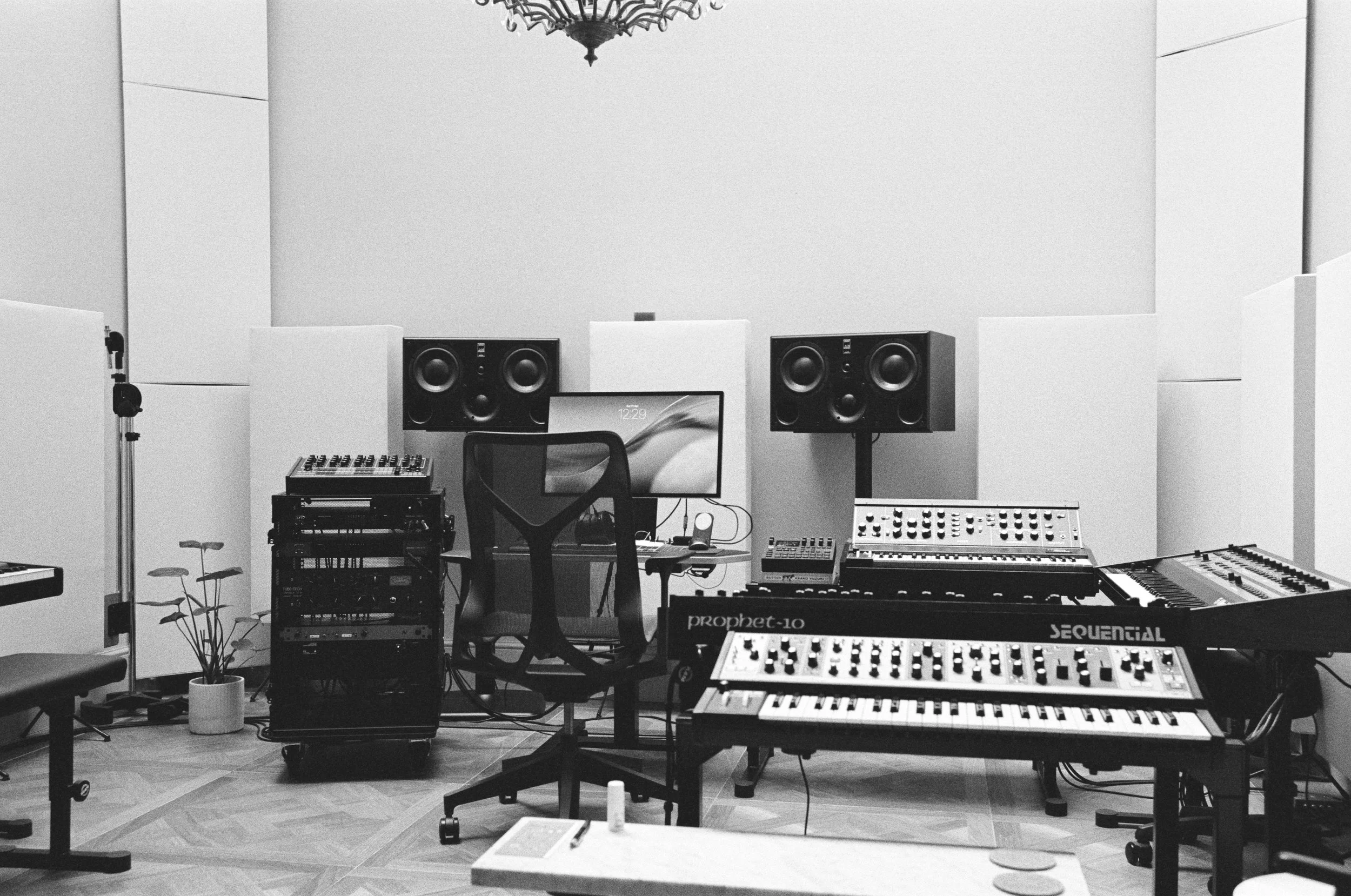 Music studio with speakers, mixing console, keyboard, computer, and microphone in a well-lit room.
