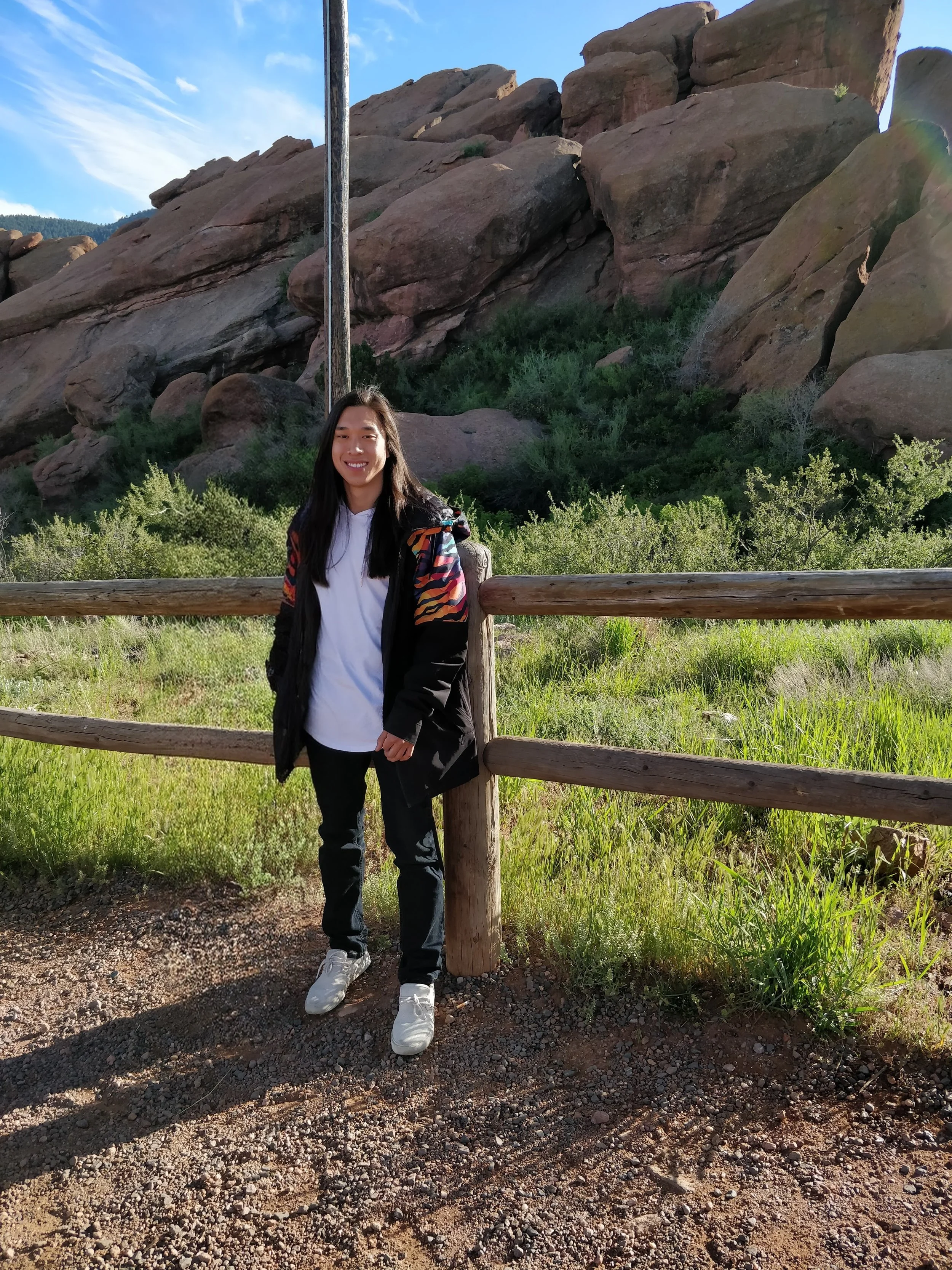 A man with long dark hair standing outside of Red Rocks Ampitheater