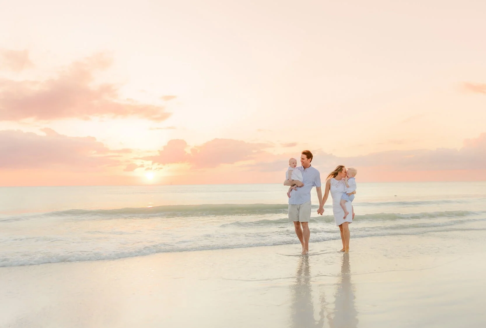 A family of four walking hand in hand on the beach during sunset, with the ocean in the background during a Naples beach portrait session.