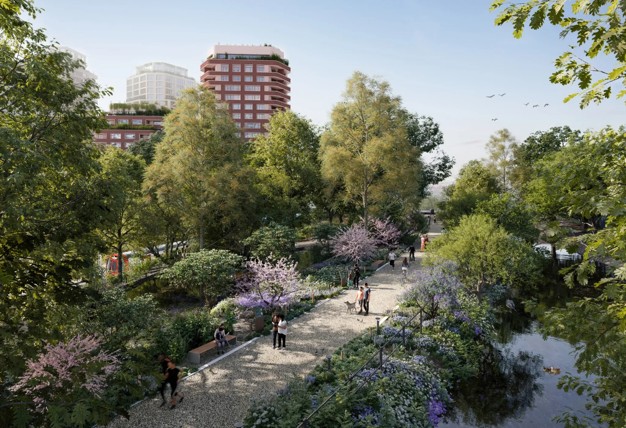 A park with blooming flowers, trees, and people walking along a gravel path, with modern buildings in the background under a clear blue sky.