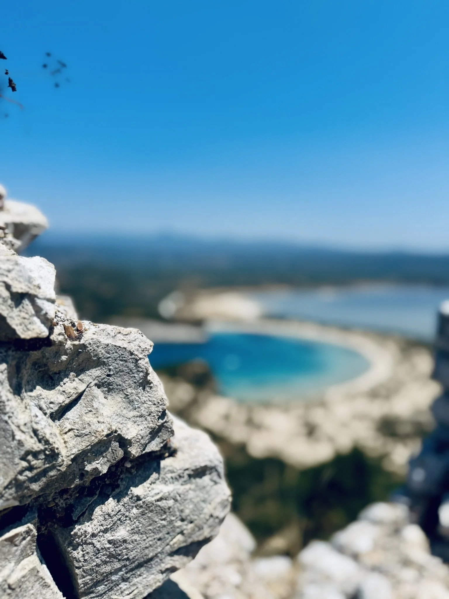 Felsen im Vordergrund, Wasser und Strand in der Hintergrund, blauer Himmel.
