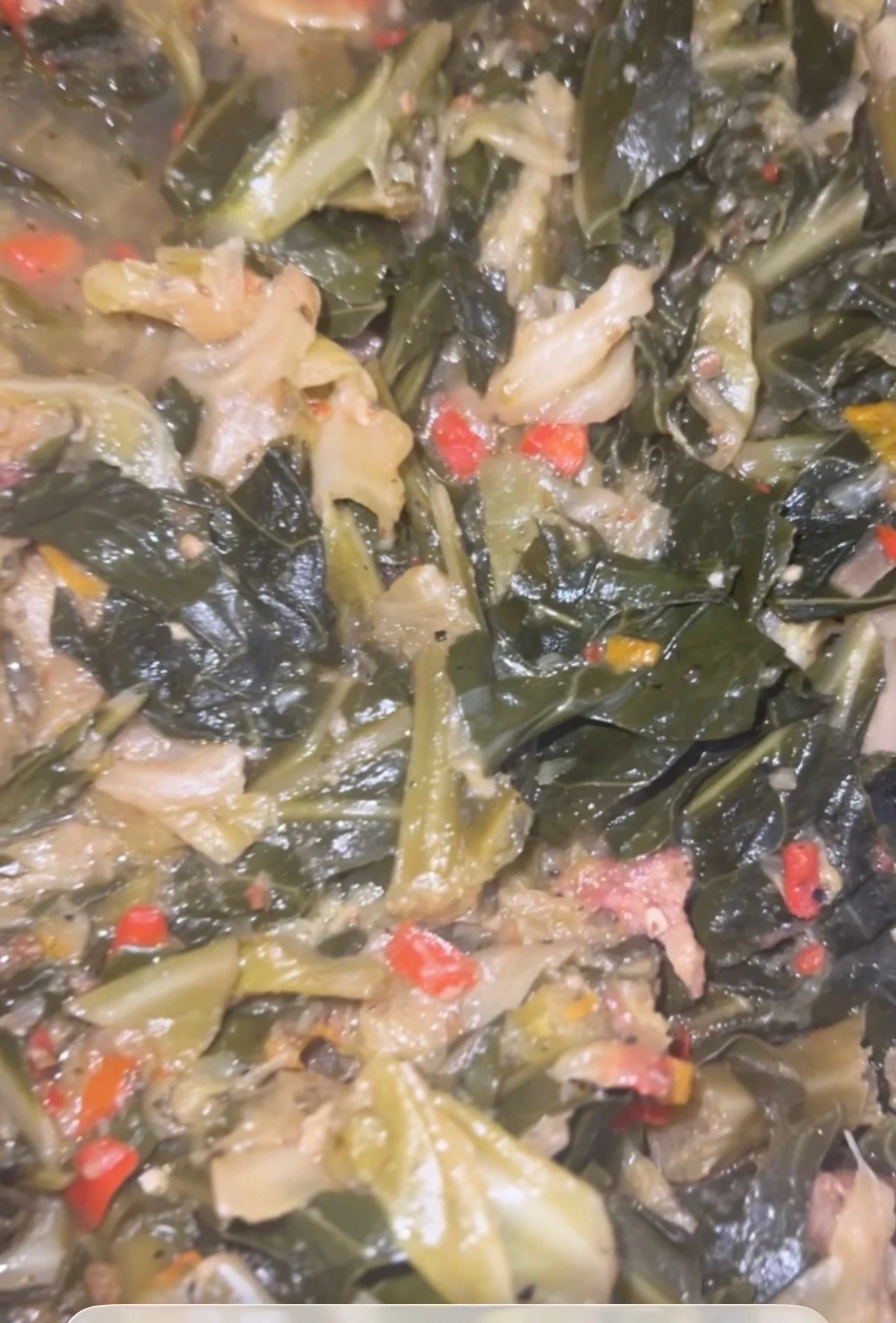 Close-up of cooked greens with bits of red and yellow, possibly hot peppers or carrots.