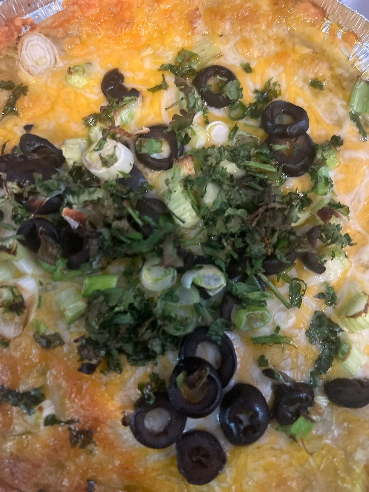 Close-up of a cheesy casserole with sliced black olives, chopped green onions, and chopped cilantro on top.