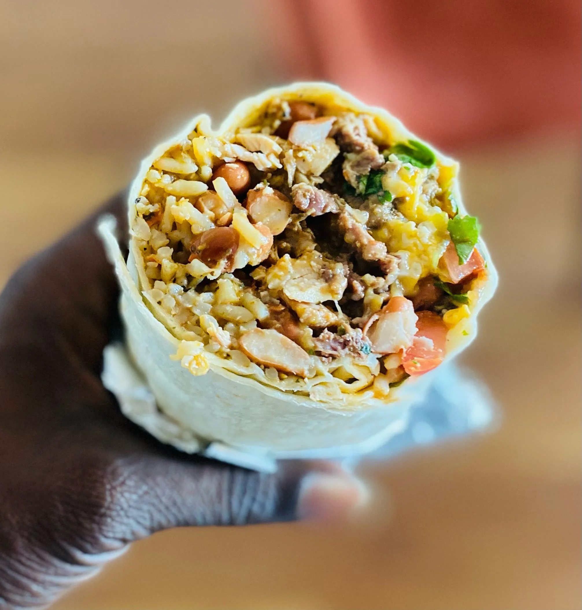 Close-up of a burrito filled with rice, beans, meat, vegetables, and cheese, held in a person's hand.