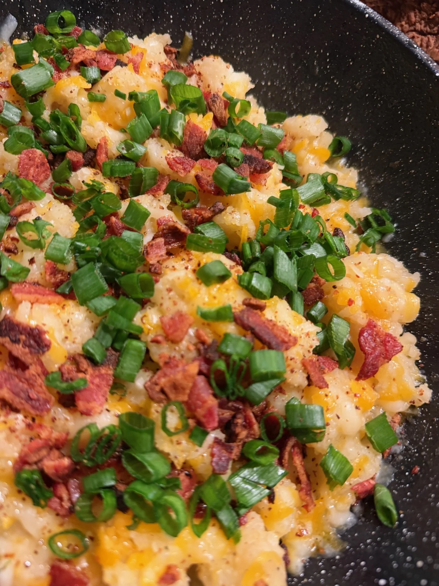 Scrambled eggs topped with chopped green onions, bacon bits, and black pepper in a black skillet.