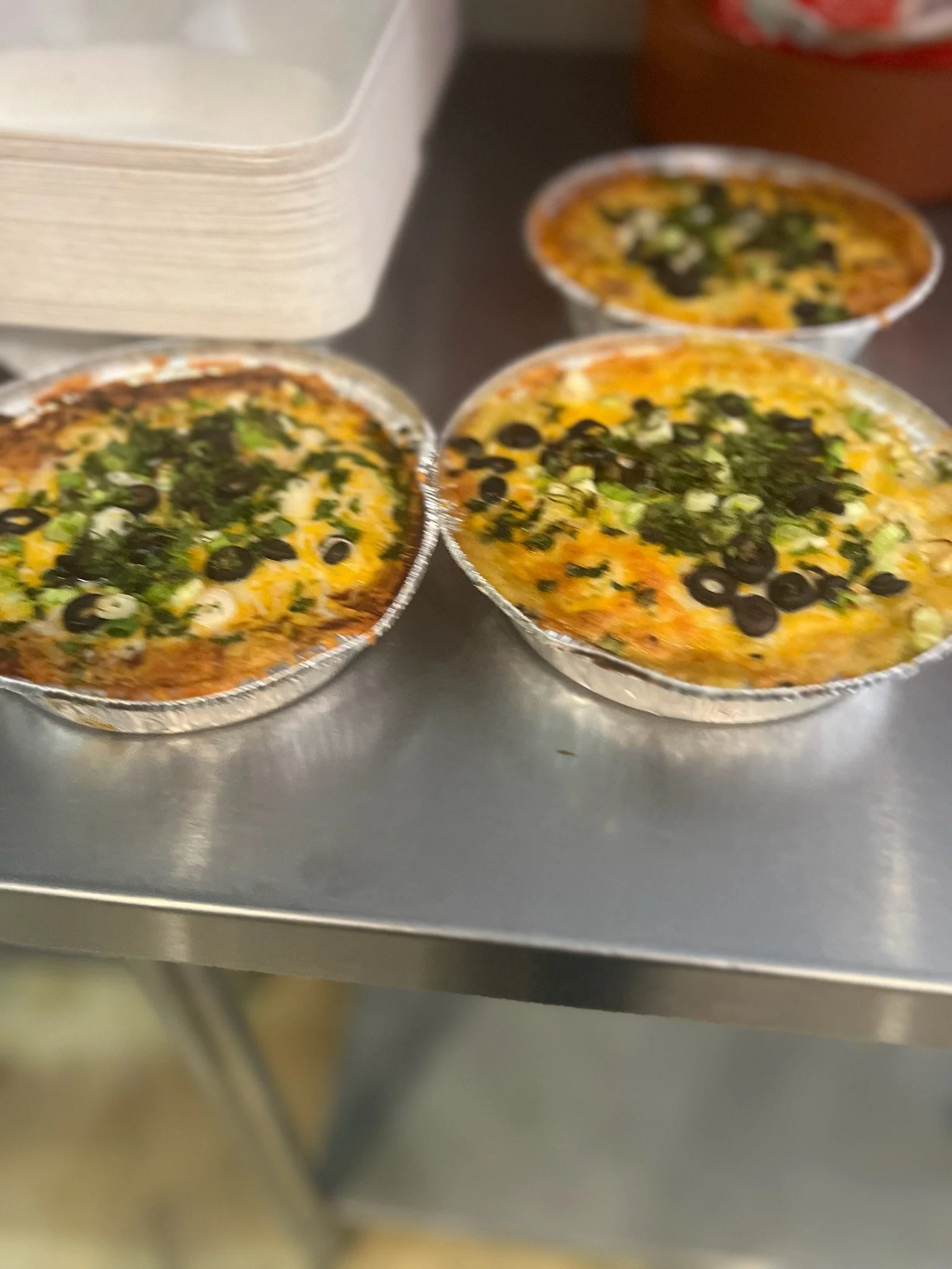 Three small aluminum foil containers filled with baked dishes topped with black olives and chopped green onions.
