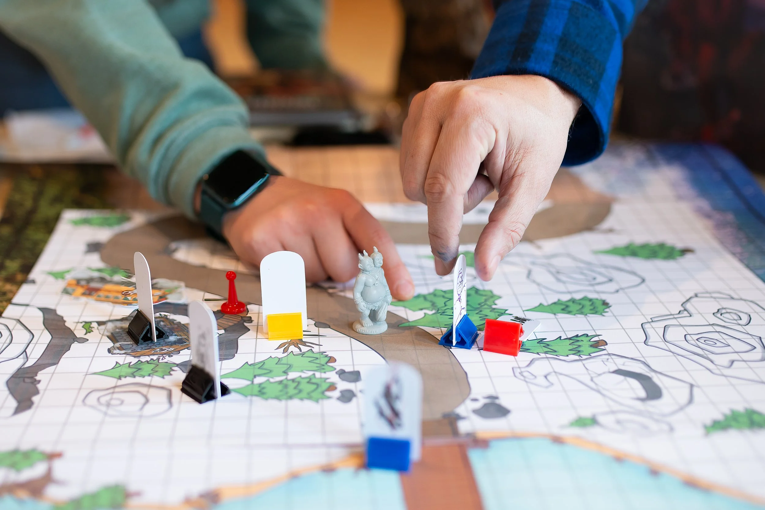 People playing a tabletop game with a colorful map, miniature figures, and game pieces such as tokens and cards.