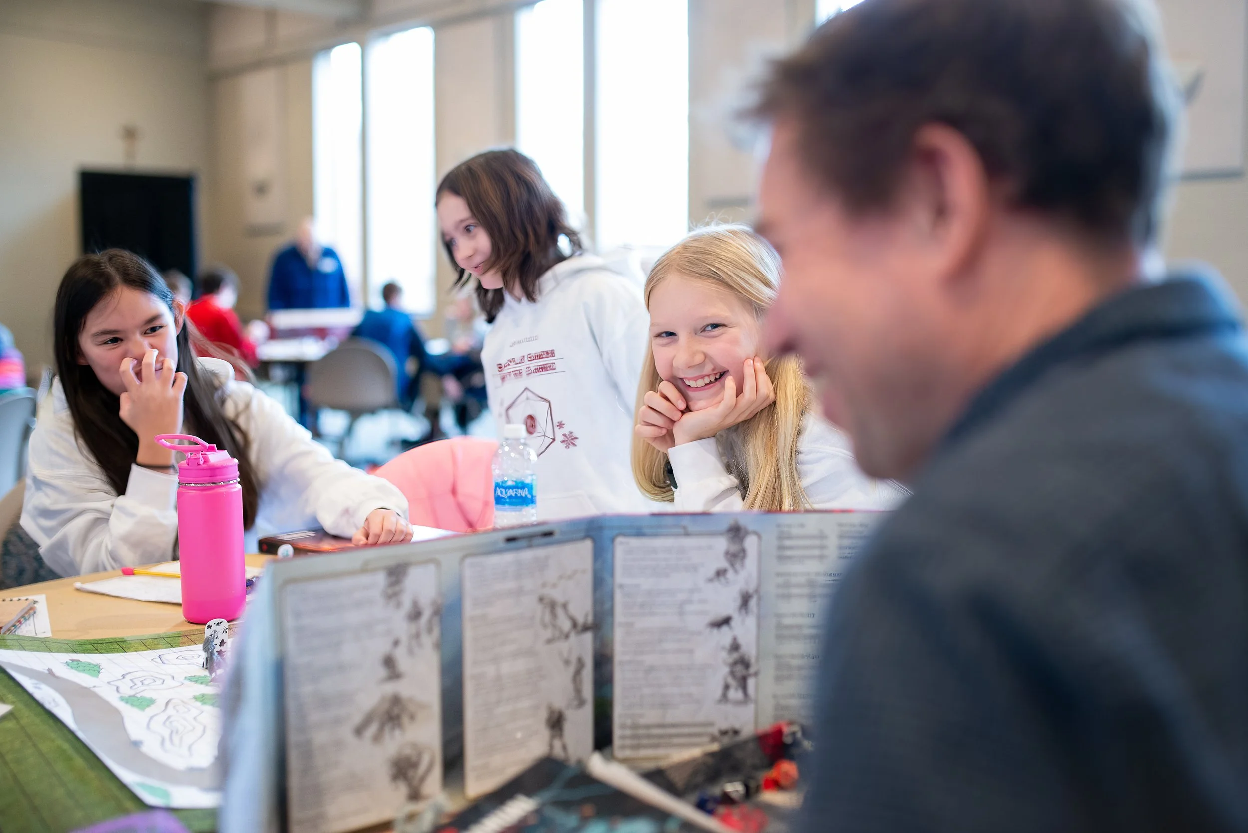 People playing tabletop role-playing game with character sheets and game materials in a classroom or community space.