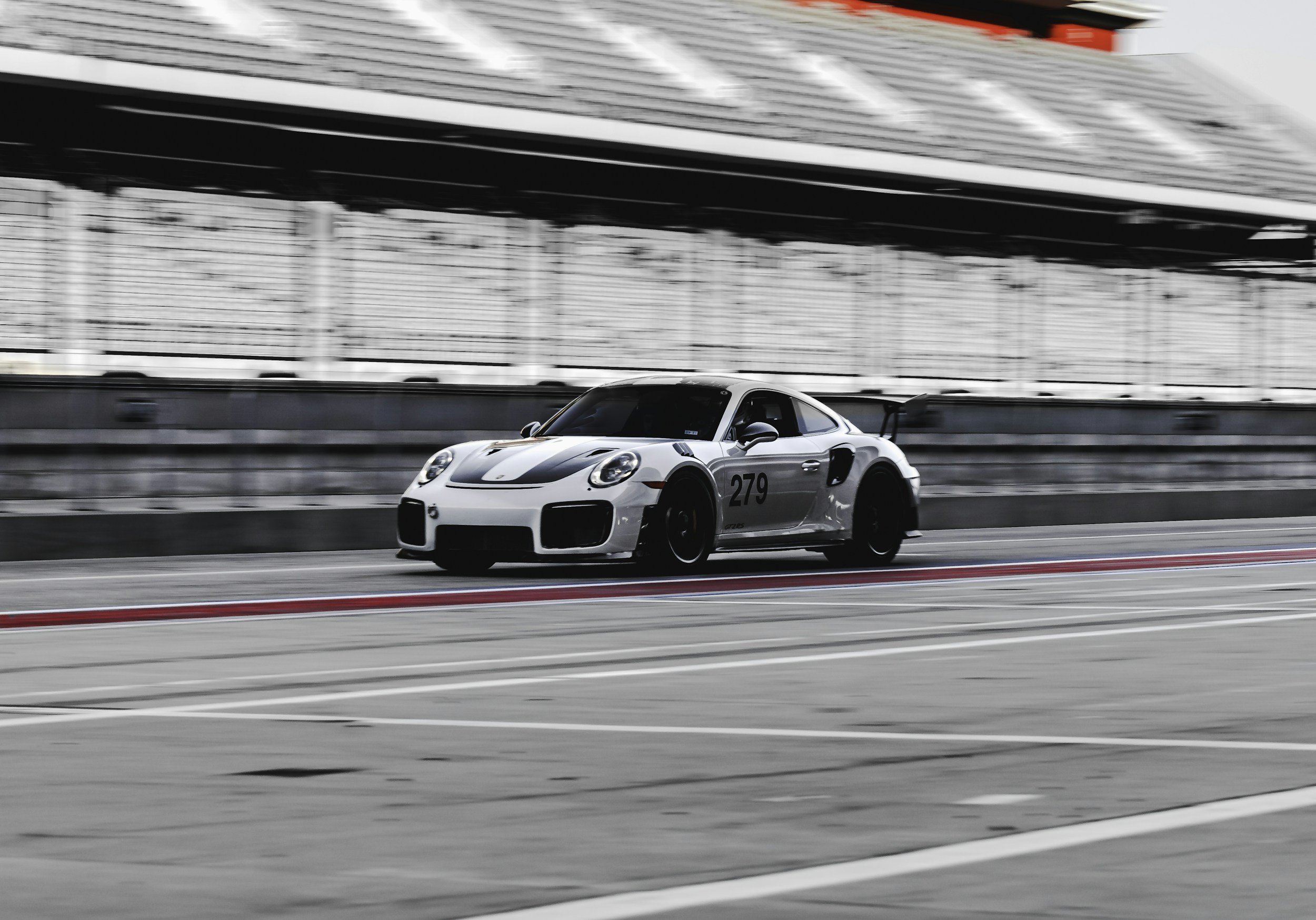 A race car driving on a race track with blurred background, black and white gradient background with some red and white painted lines on the track.