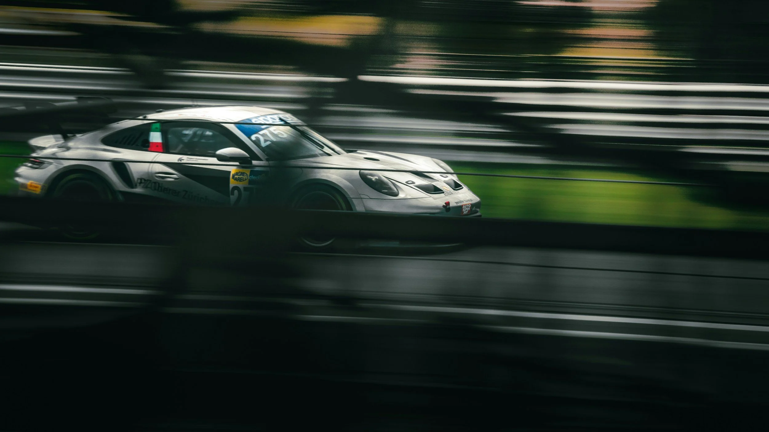 A silver race car speeding on a race track with blurred background and motion blur effect.