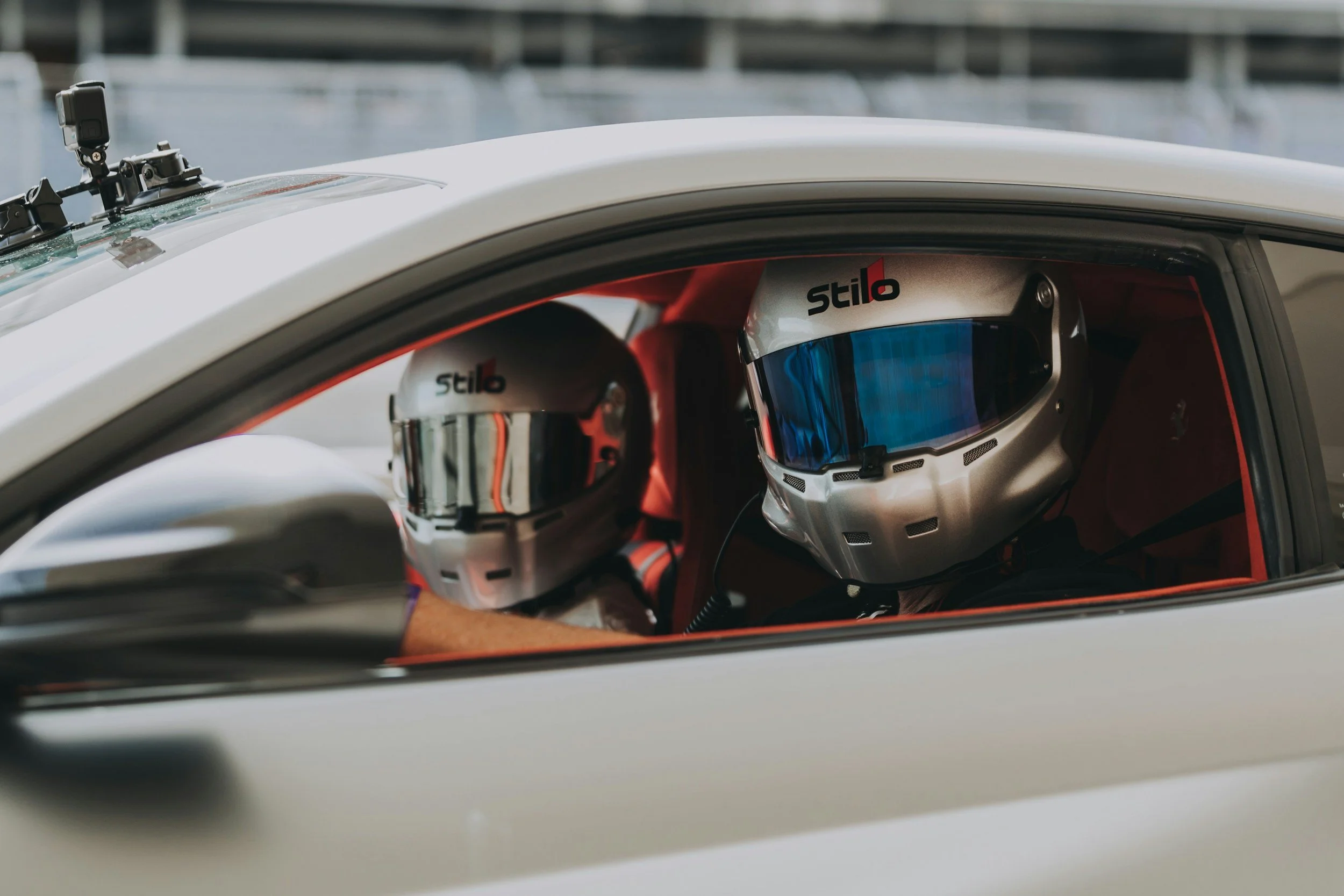 Two race car drivers wearing helmets inside a silver race car.
