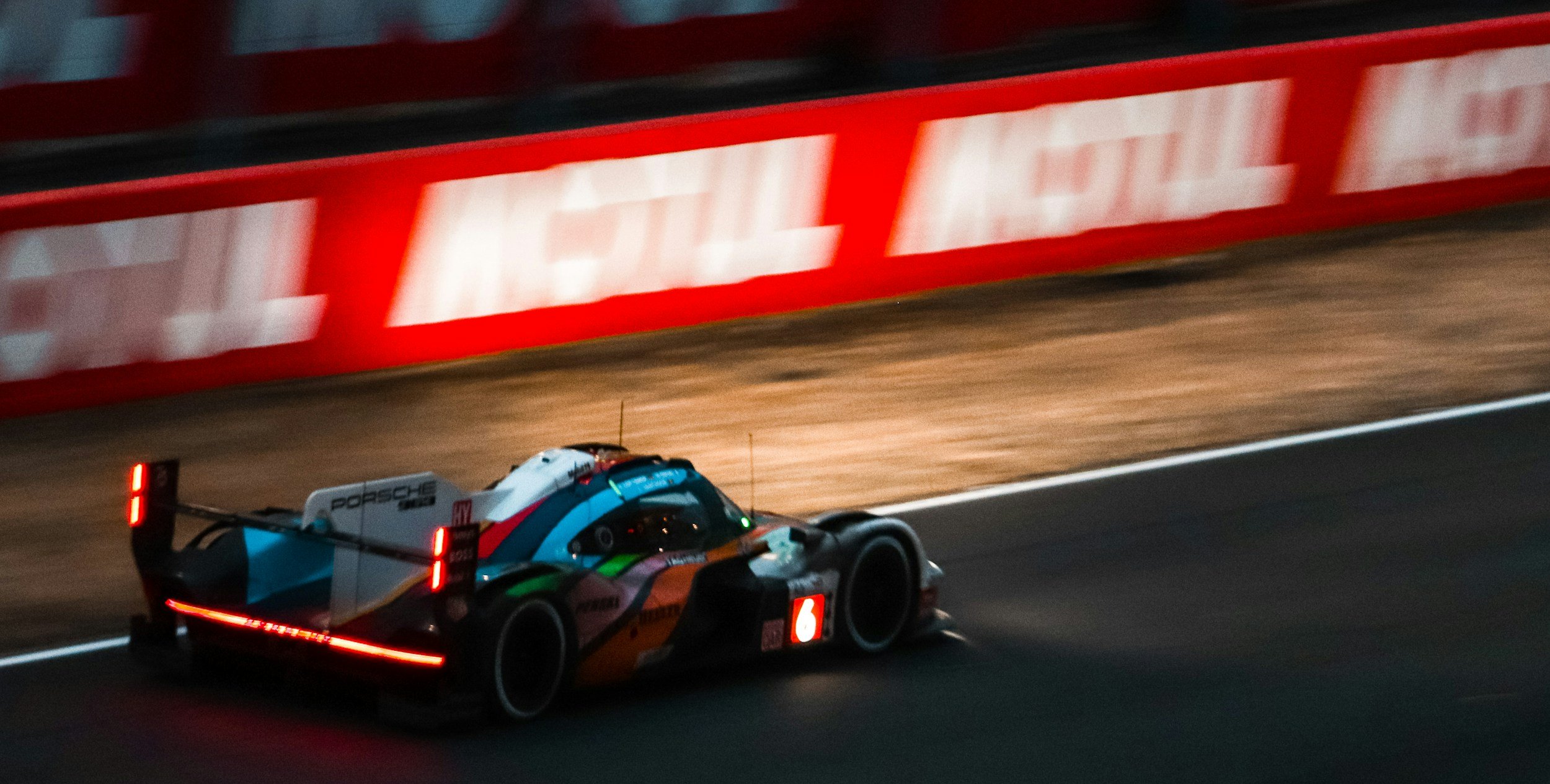 A race car driving on a track at night with a blurred background and illuminated barriers.