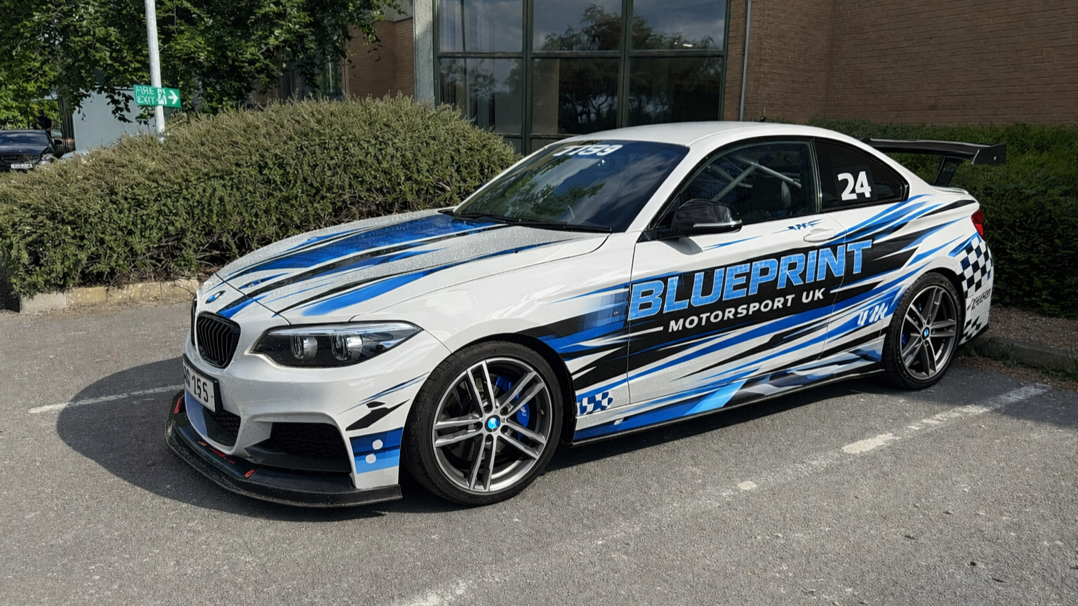 White race car with blue and black racing stripes and decals, parked in a lot.