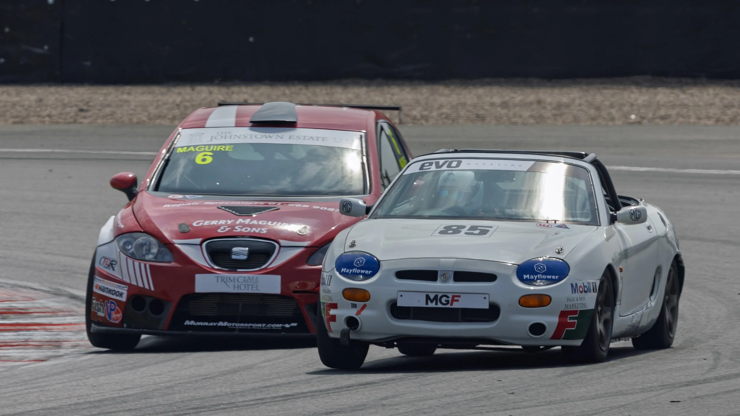 Two race cars on a track, one silver and one red, competing in a motorsport event.