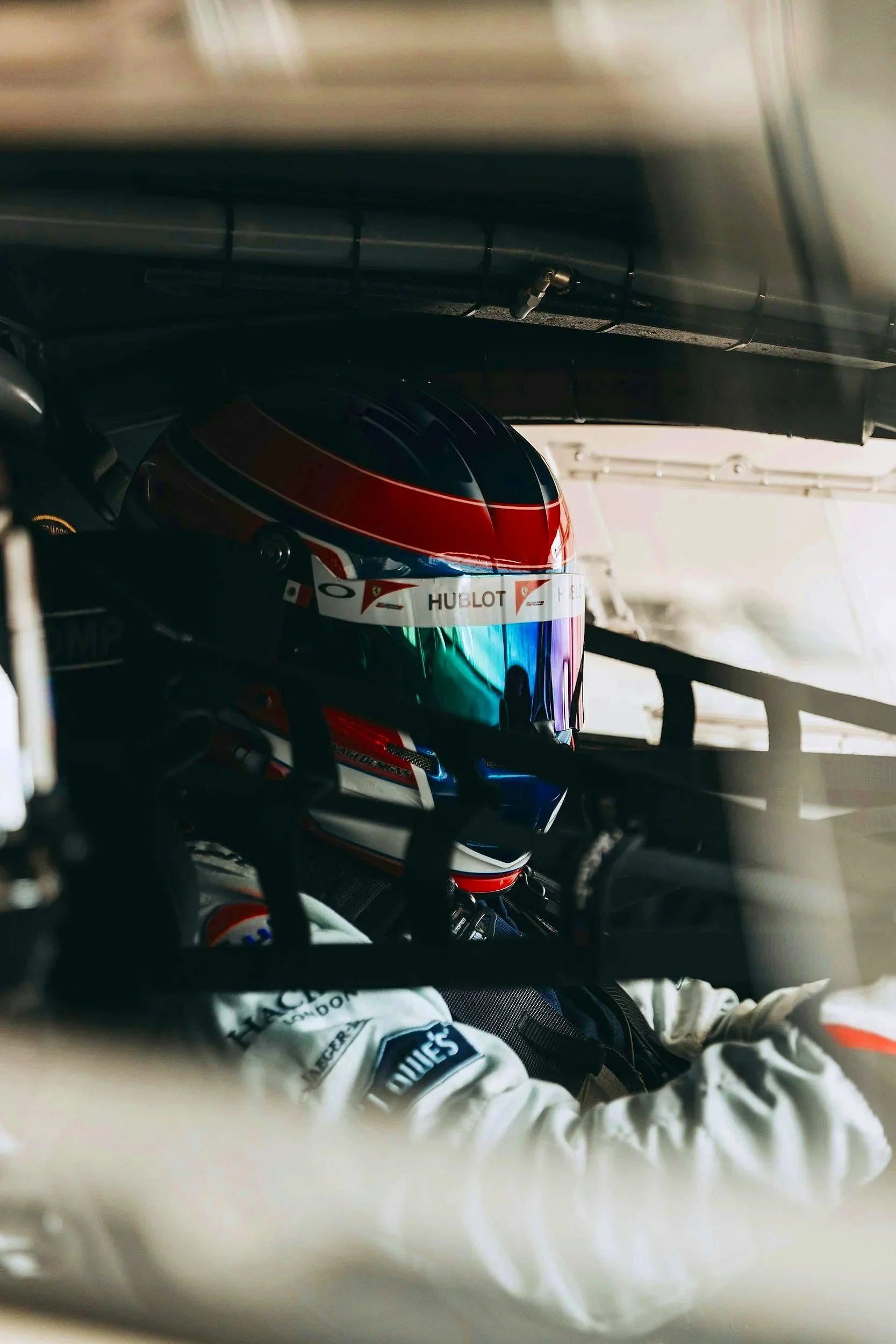 A race car driver inside the cockpit, wearing a colorful helmet and racing suit, preparing for a race.