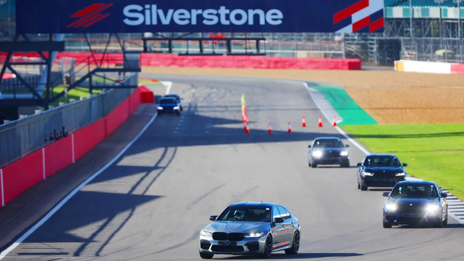 Multiple cars on a race track with a large Silverstone banner overhead.