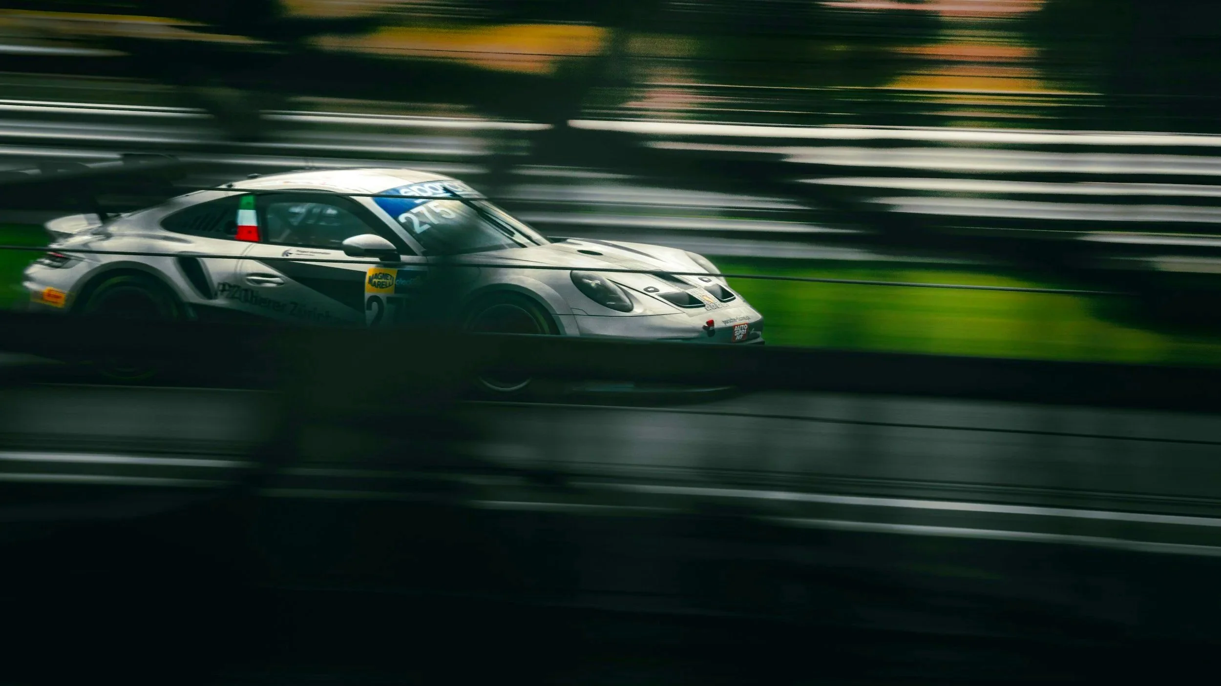 A silver race car speeding on a racetrack with motion blur, surrounded by blurred background.