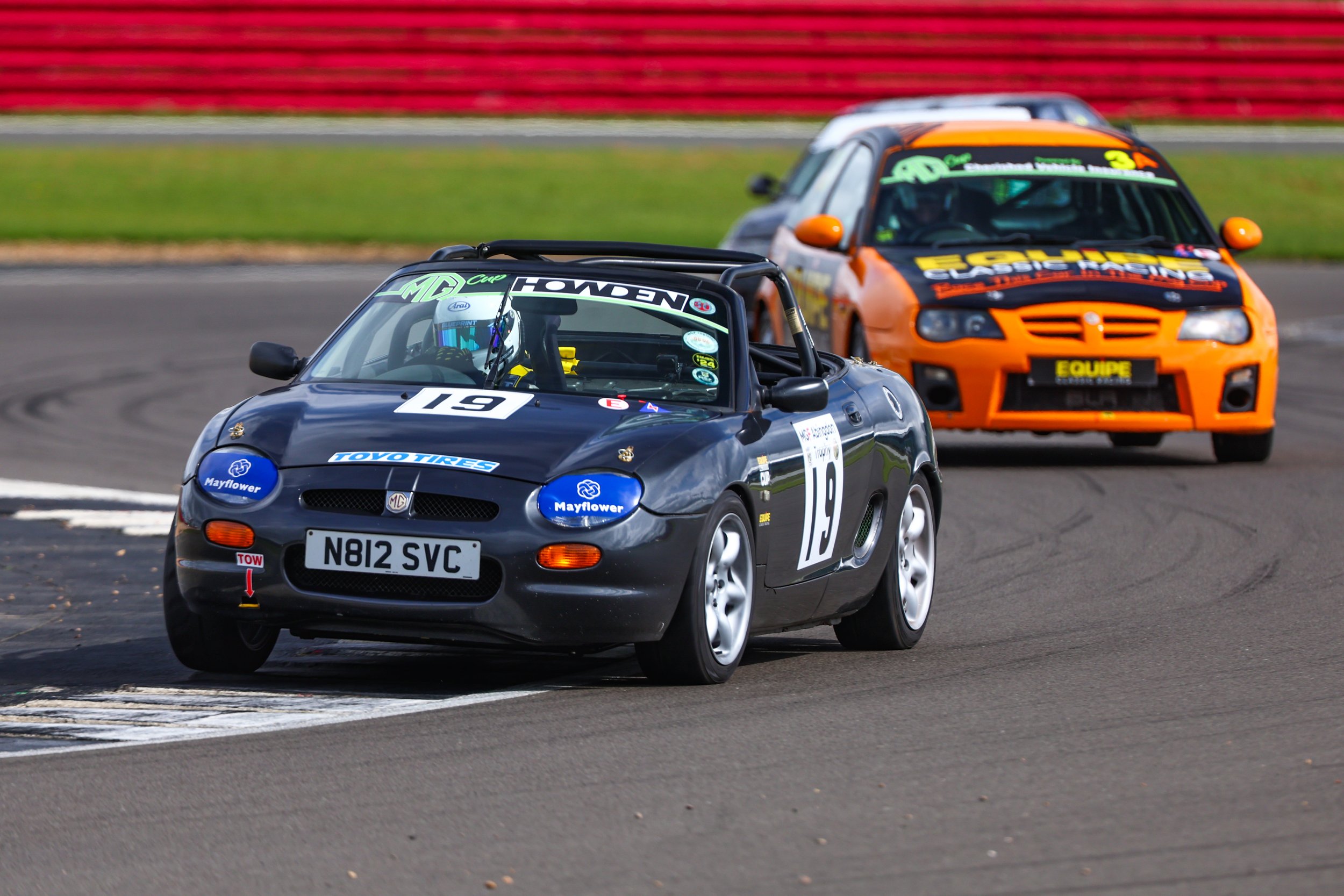 Two race cars on a track, one red with the number 6 and the other white with the number 85, racing closely against each other.