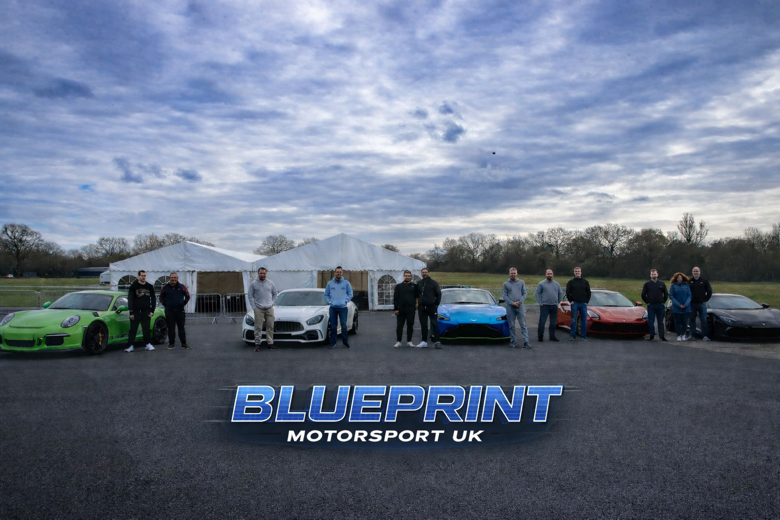 Lineup of nine people standing next to luxury sports cars including a green Porsche, a white Mercedes, a blue Aston Martin, a red Ferrari, and a black Lamborghini, with tents and trees in the background, and a large blue 'BLUEPRINT MOTORSPORT UK' logo in the foreground.
