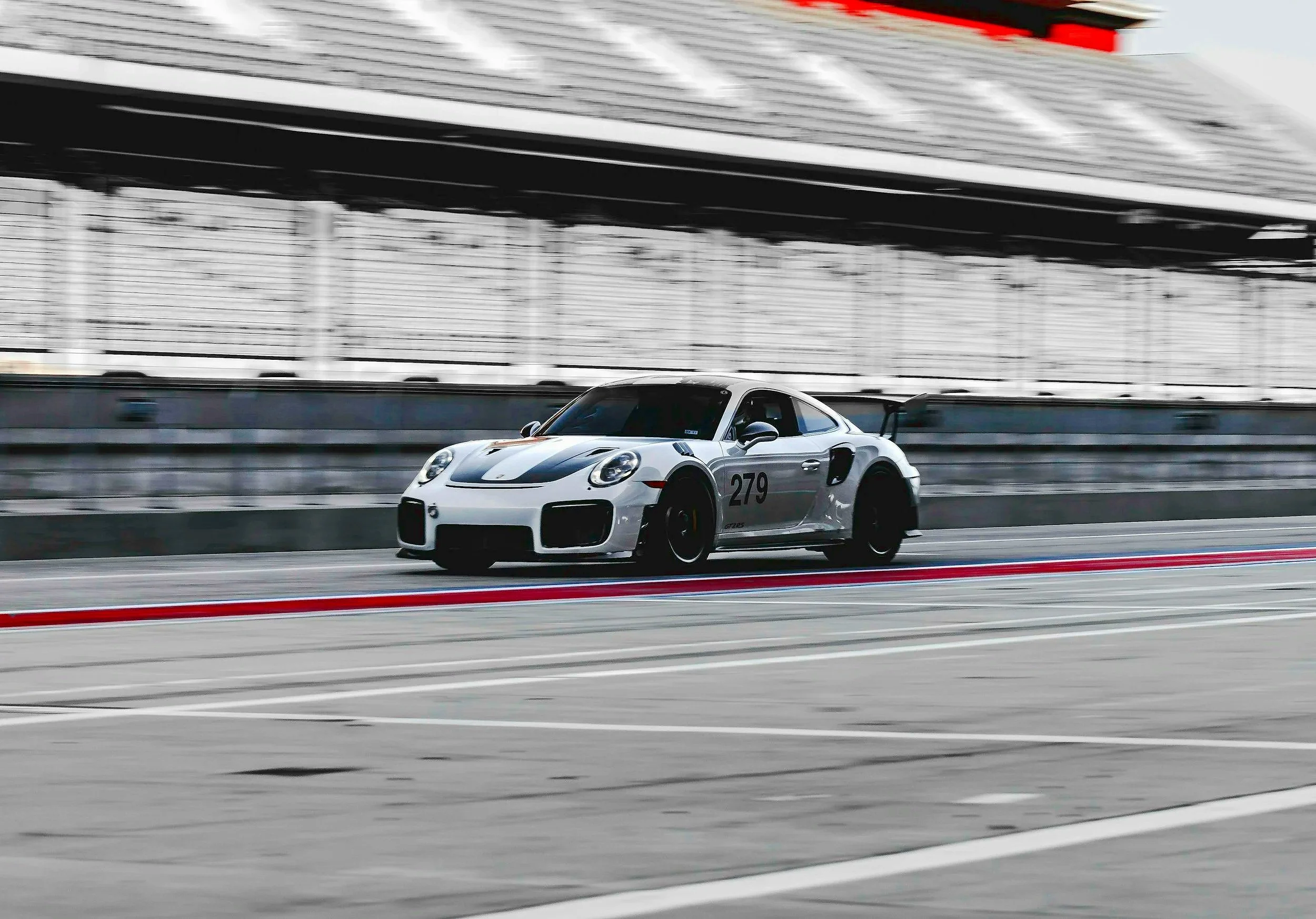 A porsche race car with black and orange accents speeding on a race track.