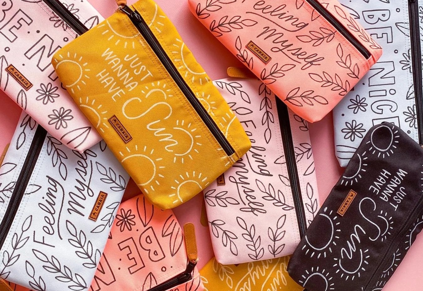 A collection of colorful pencil cases with inspirational and motivational phrases on a pink background.