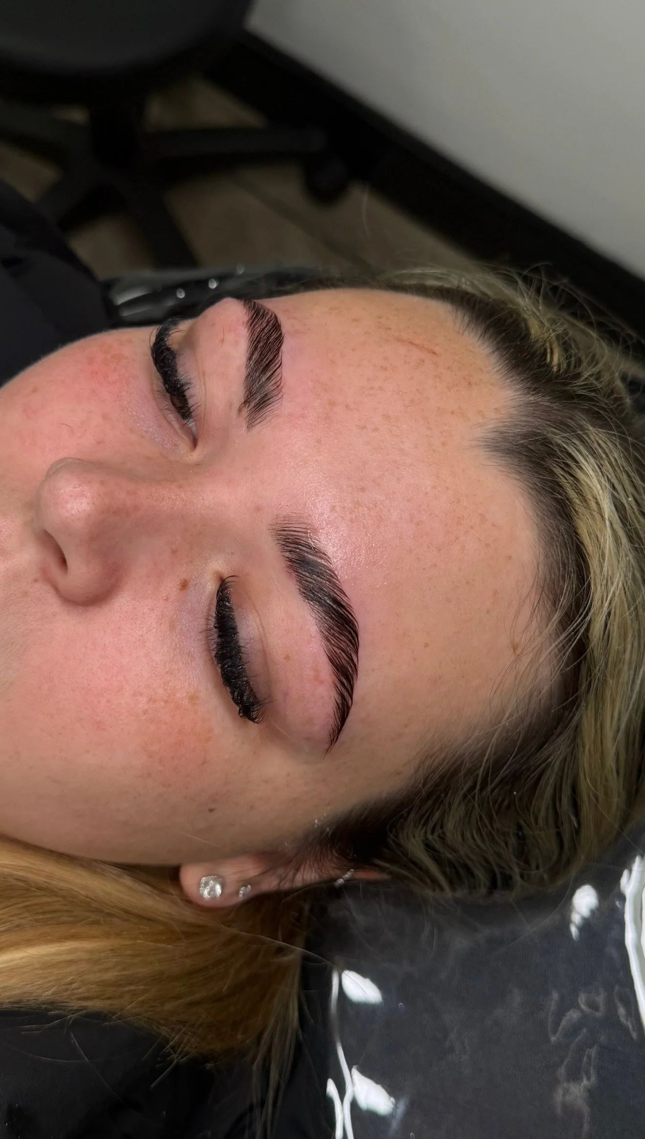 Close-up of a woman's face with freshly done eyelash extensions and well-groomed eyebrows, lying down with her eyes closed.