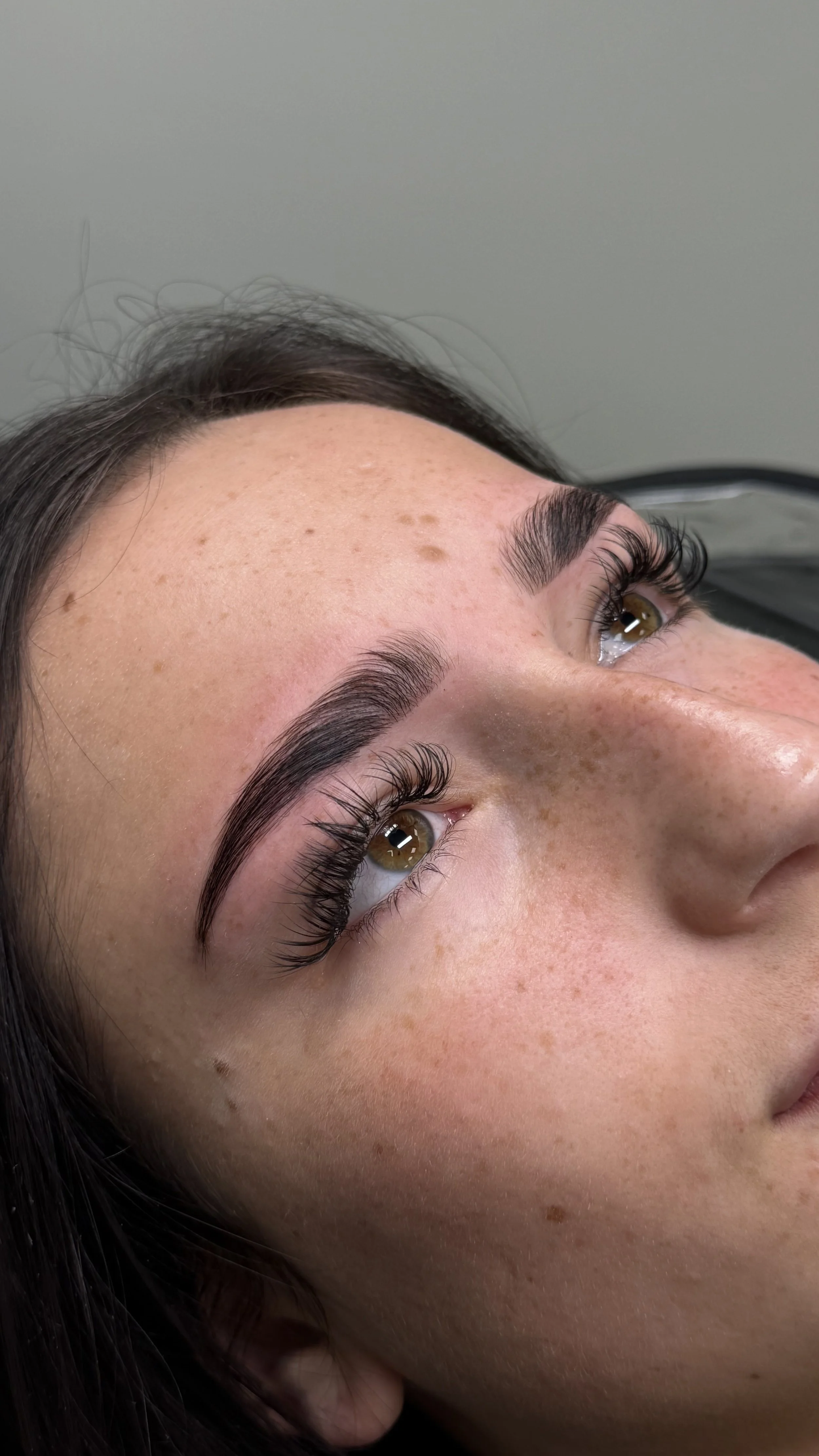 Close-up of a woman's face showing her well-groomed eyebrows, long eyelashes, and clear skin with freckles.