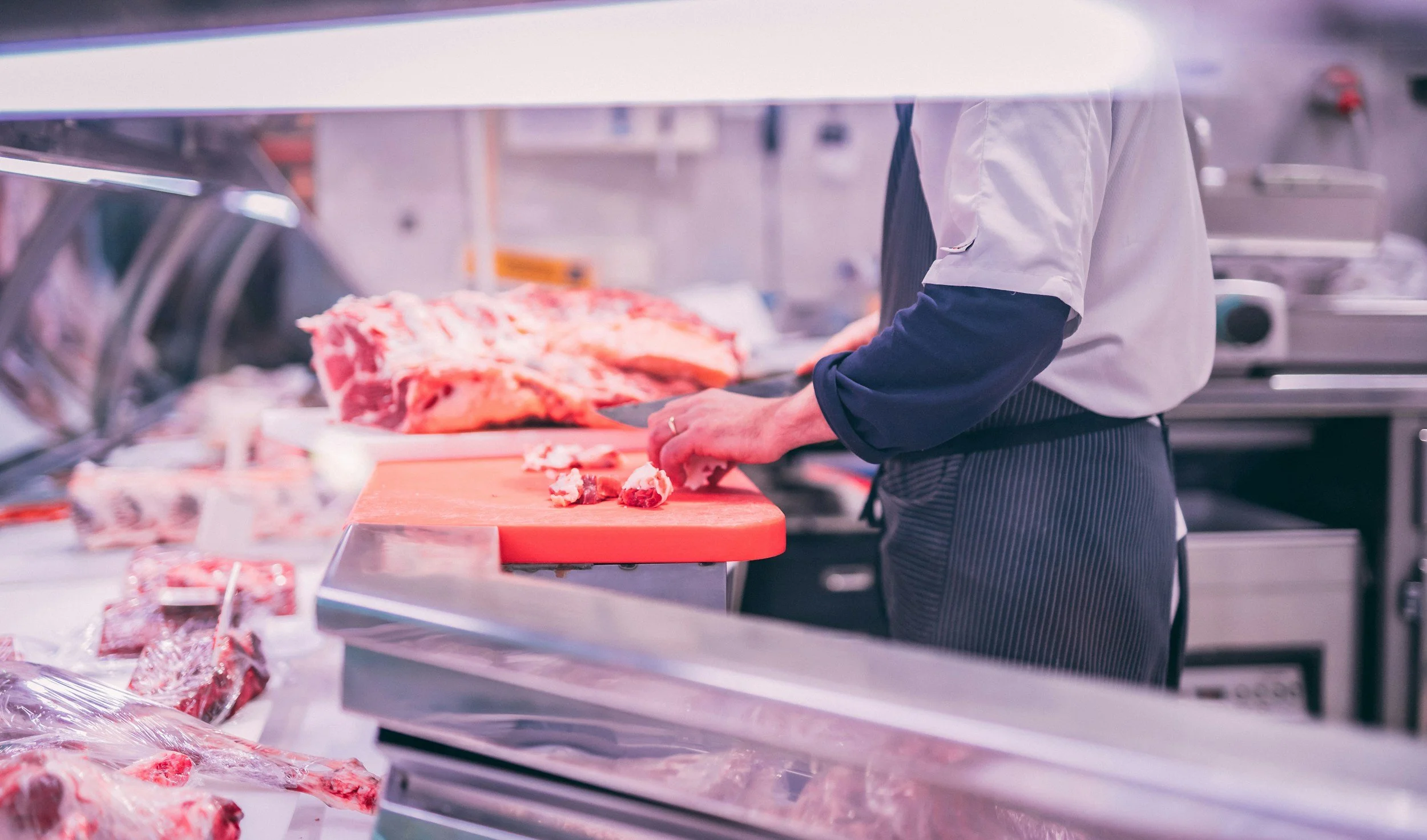 Butcher slicing meat on a cutting board in a meat shop.
