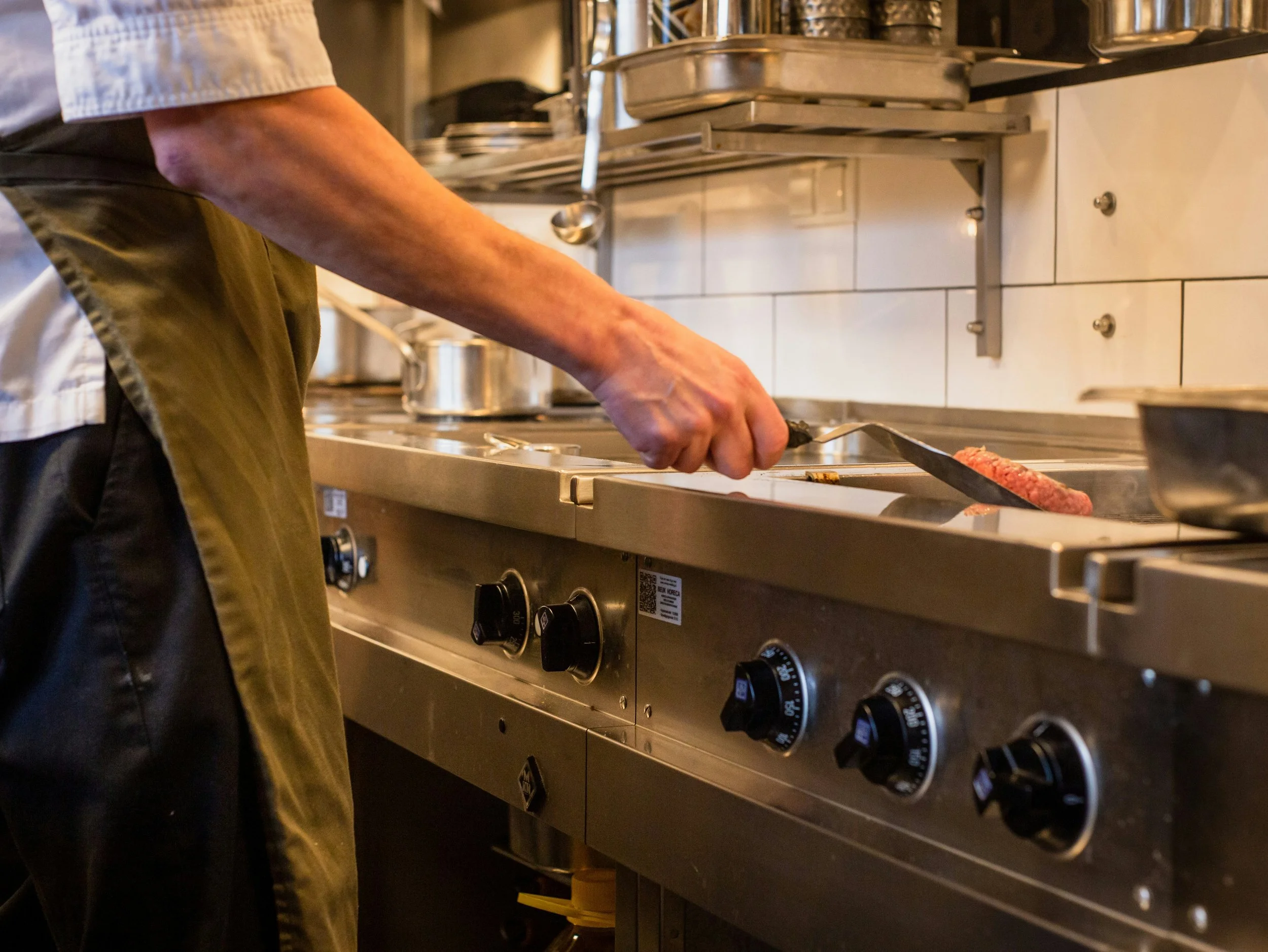 Person cooking a hamburger patty on a commercial stove in a restaurant kitchen.