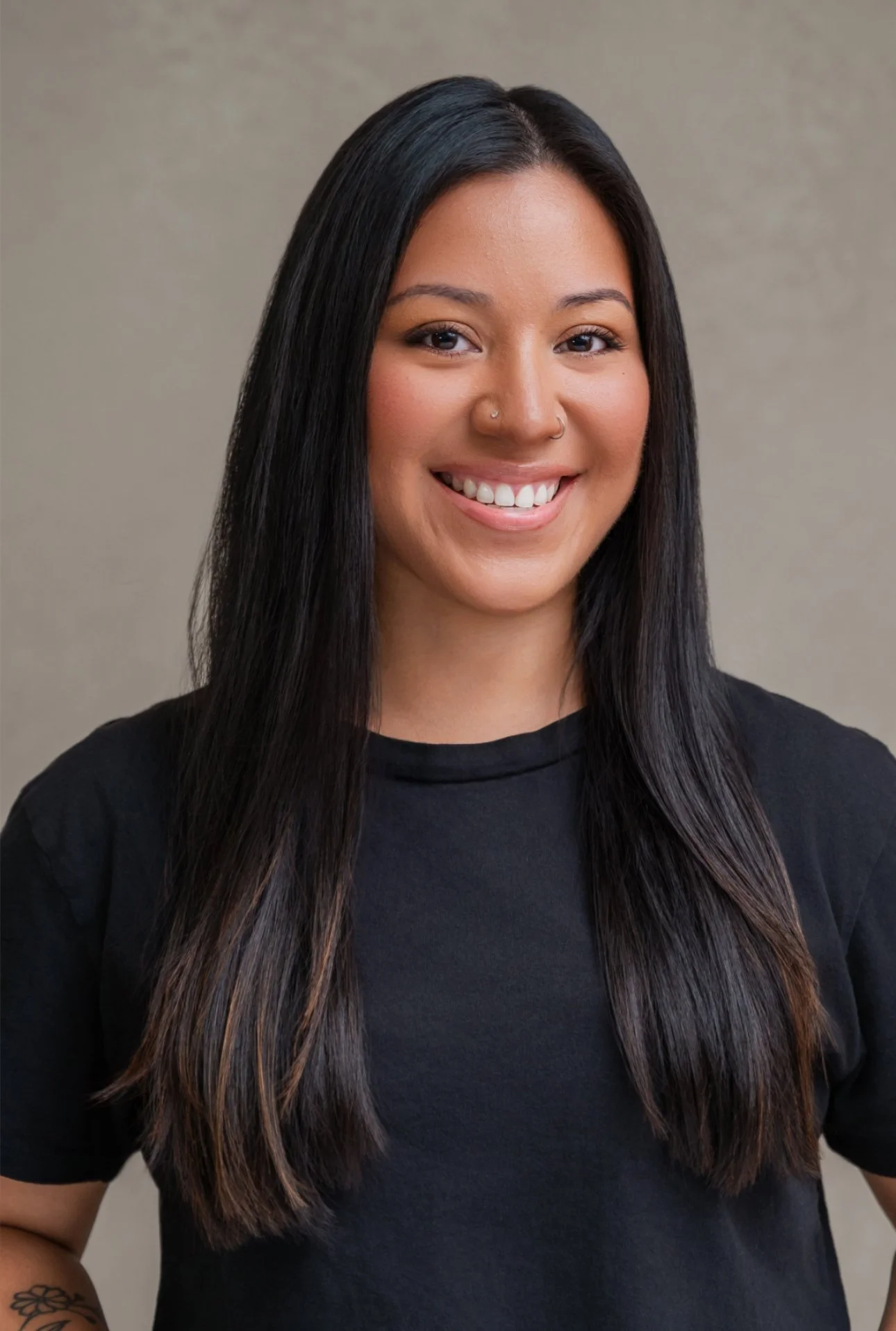 A woman with long, dark hair smiling at the camera, wearing a black t-shirt, with a neutral background.