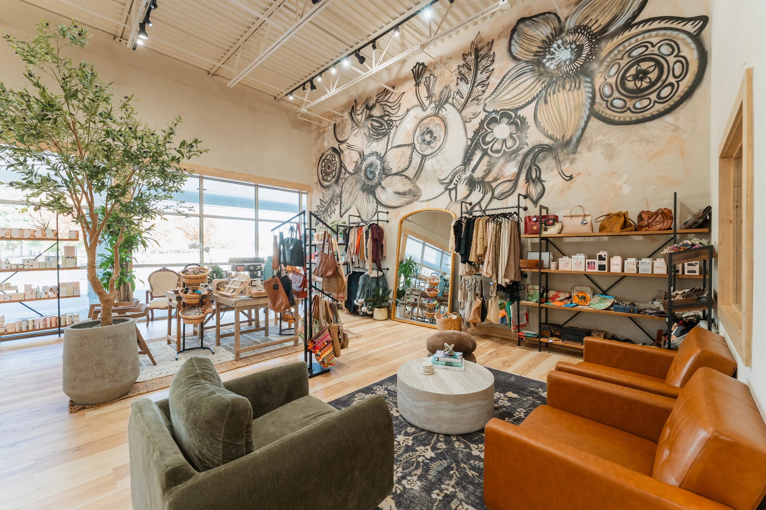 Interior of a boutique store with a large mural of flowers on the wall, displaying clothing, bags, and accessories, along with seating area.