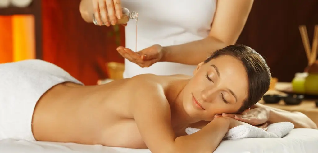 A woman receiving a massage with oil in a spa setting, lying face down with eyes closed.