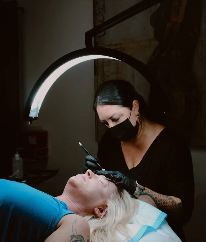 A woman getting a beauty treatment or tattoo on her face by a professional in a clinic setting.