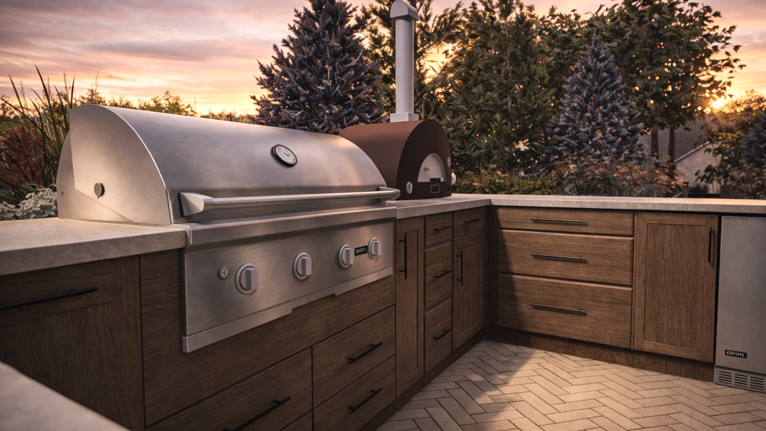 Outdoor kitchen with stainless steel grill and pizza oven at sunset, surrounded by trees and foliage.