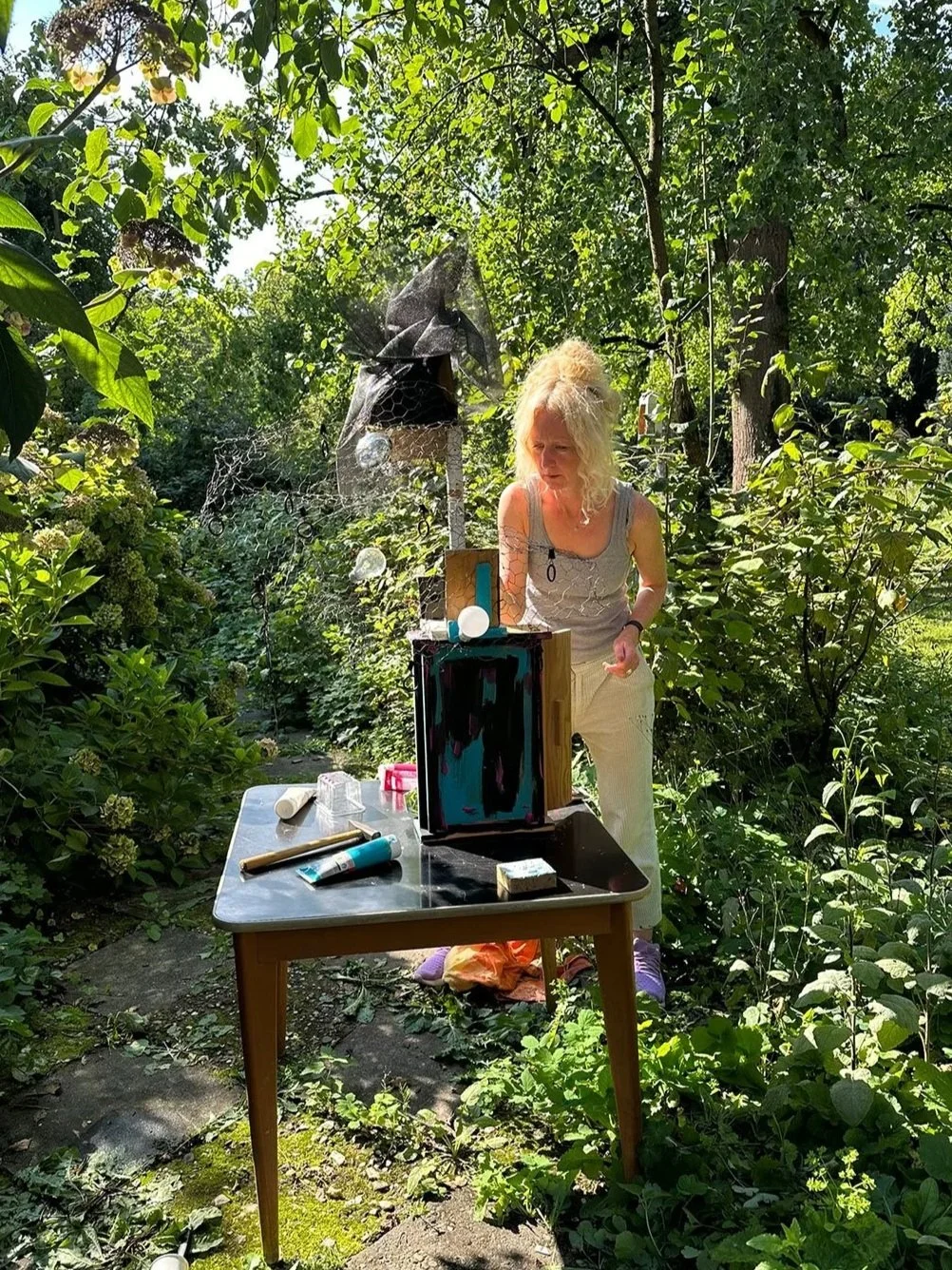 Person creating a mixed-media artwork outdoors using recycled materials and tools on a table