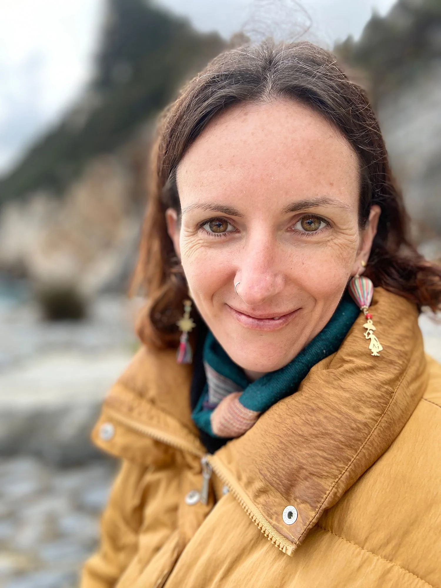 Portrait of the Gestaltete Interaktion workshop facilitator smiling outdoors, wearing colourful earrings and a warm jacket