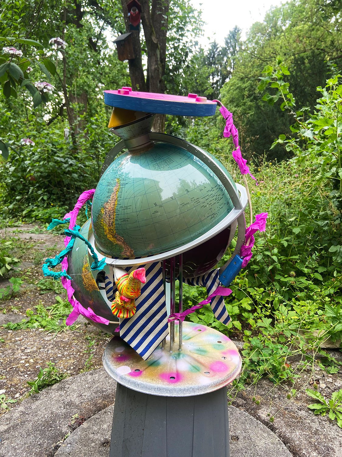 Playful sculpture made from a globe and repurposed materials, decorated with colourful elements outdoors