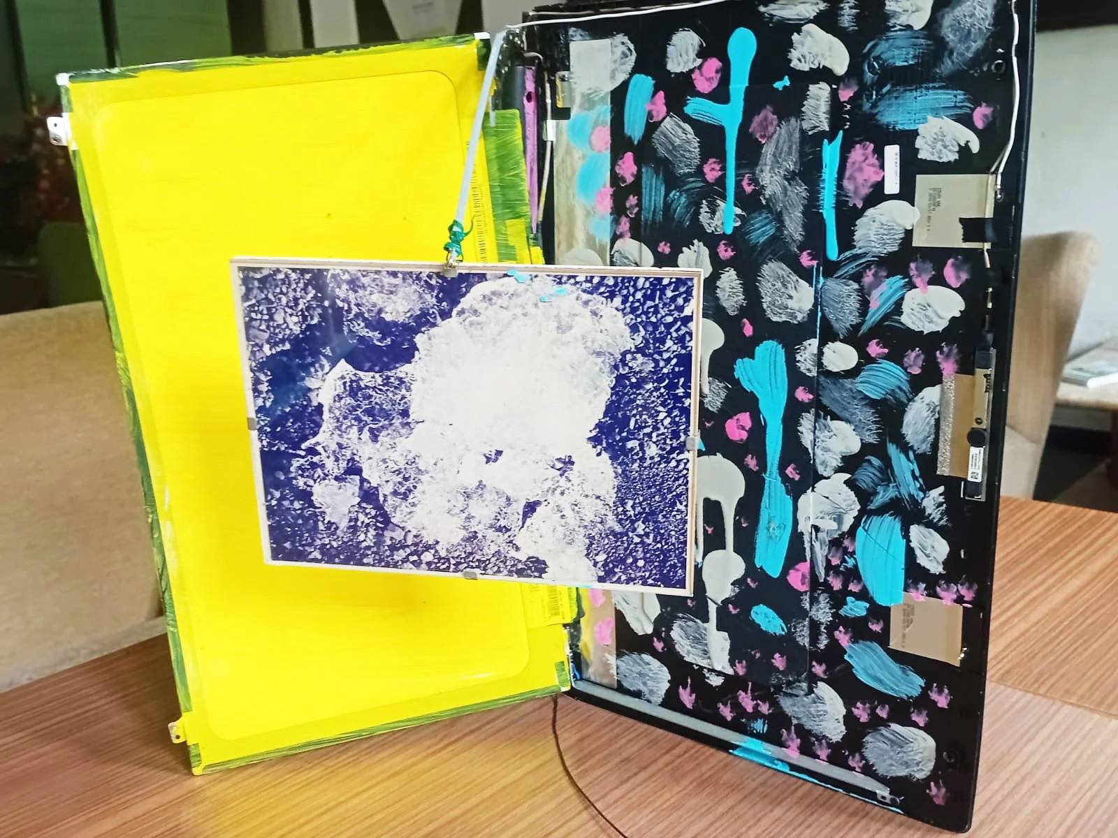 Mixed-media artwork created from a disassembled laptop, featuring bright colours and abstract textures inside the case