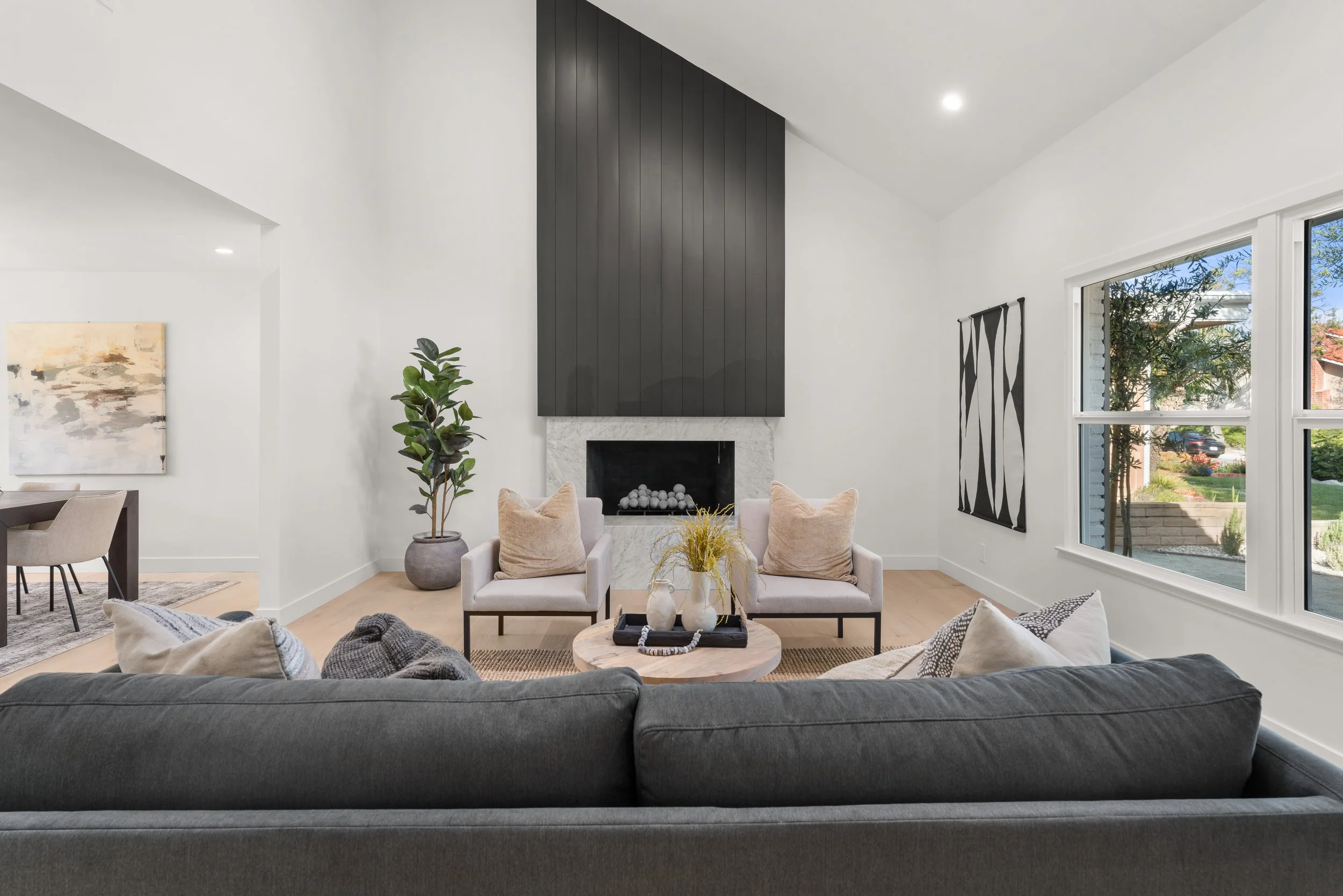 Living room with a fireplace, two armchairs, a sofa, a coffee table, large windows, and modern wall art.