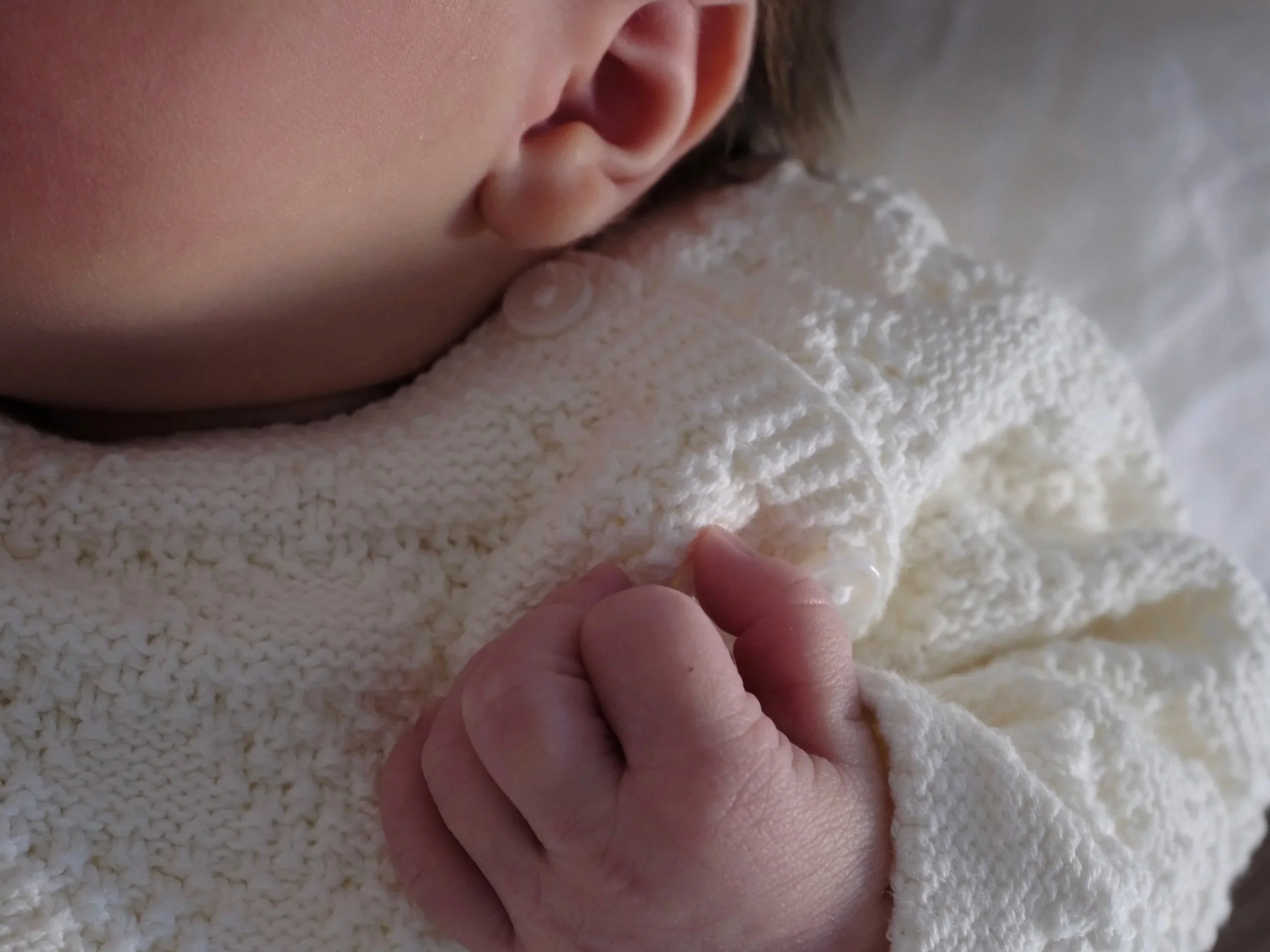 Close-up of a person's ear and part of their face, with a hand touching or holding a soft, textured white towel.
