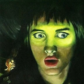 A woman with dark hair and wide eyes looks surprised or shocked; her face is illuminated with a greenish light.